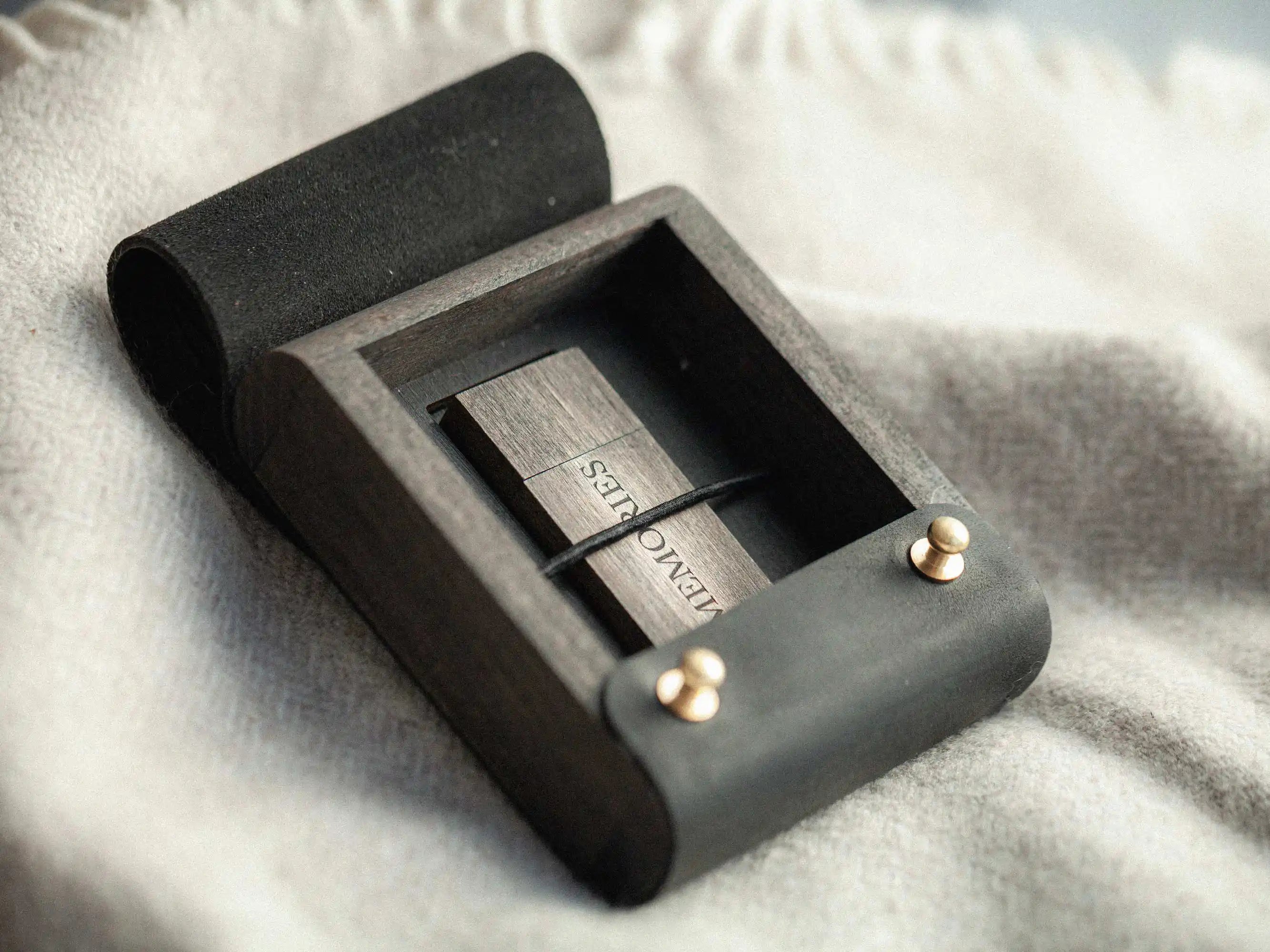 Open black leather and wood USB box with wooden USB drive under elastic strap