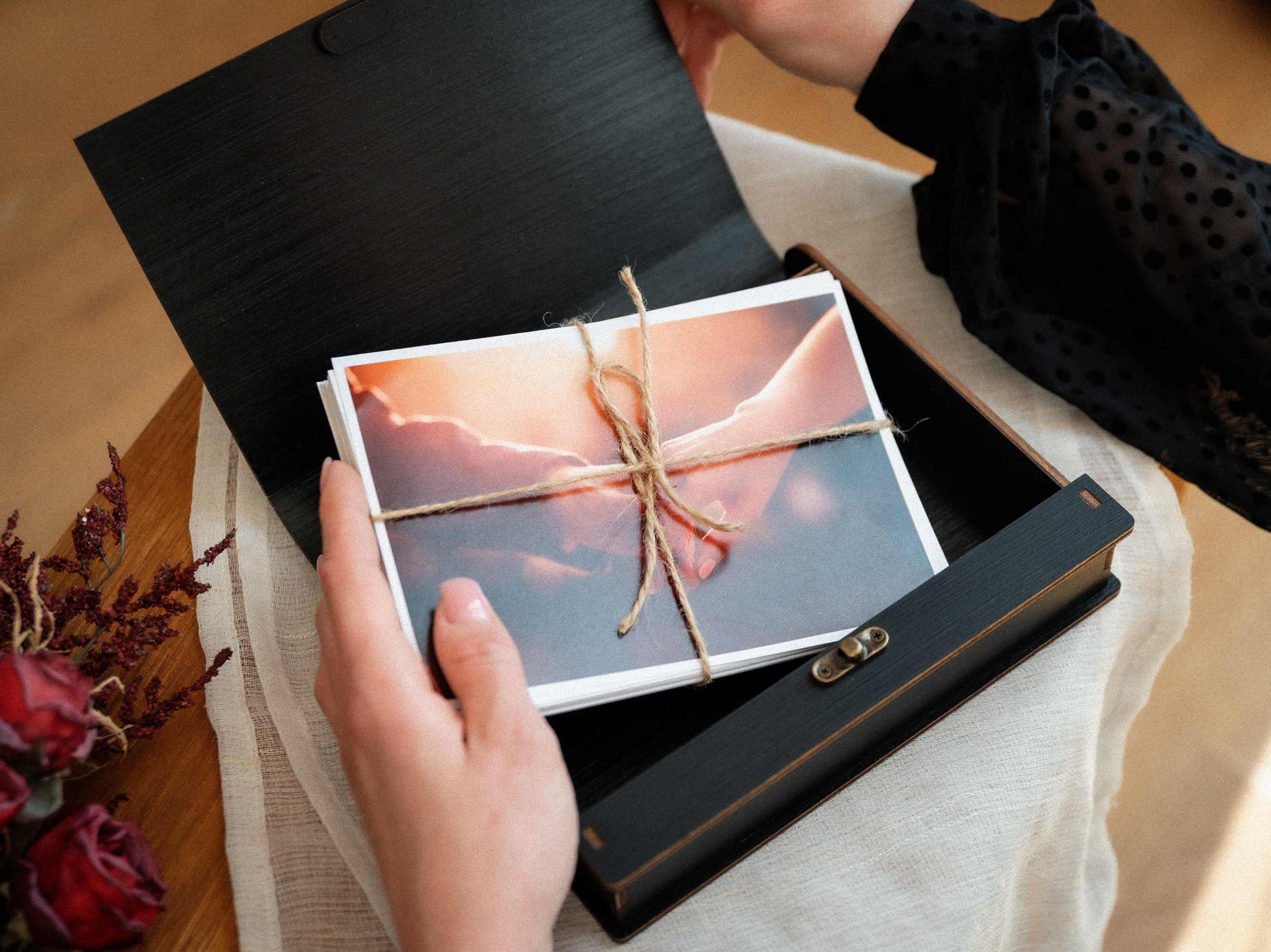 Open black wooden photo box with wedding prints tied with linen cord