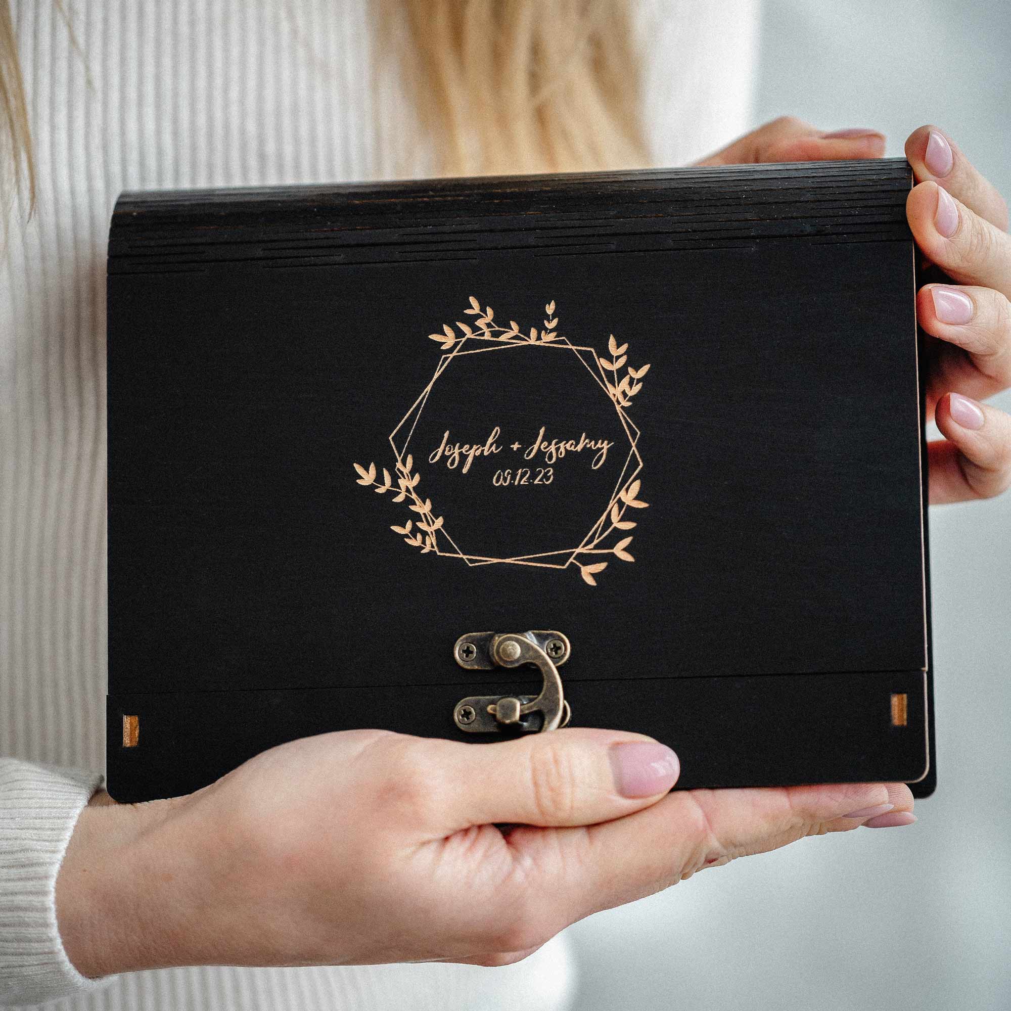 Hands holding personalized black wooden photo box with engraving, front view, photographer client gift