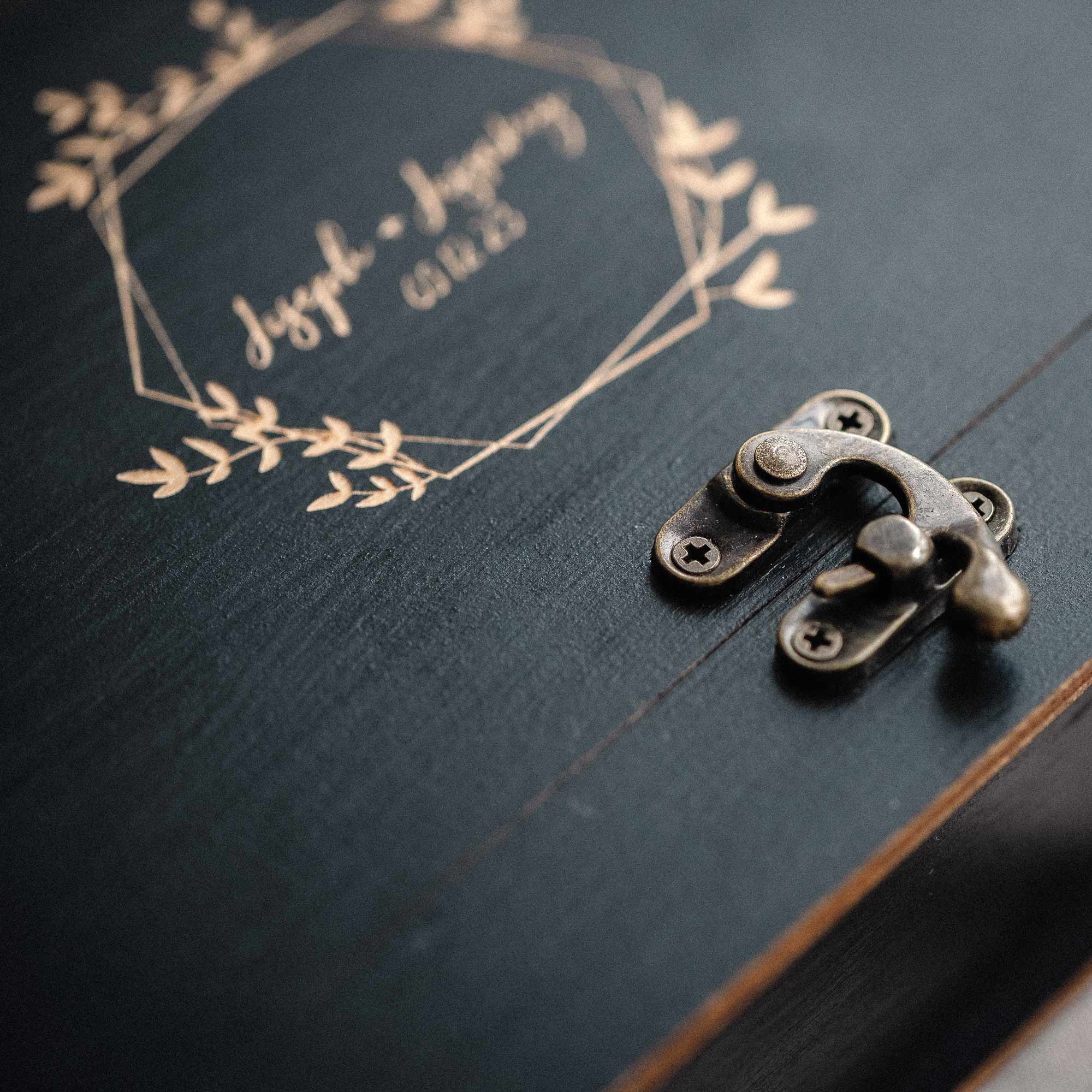 Close-up of vintage metal latch on black wooden photo box with engraved wreath design