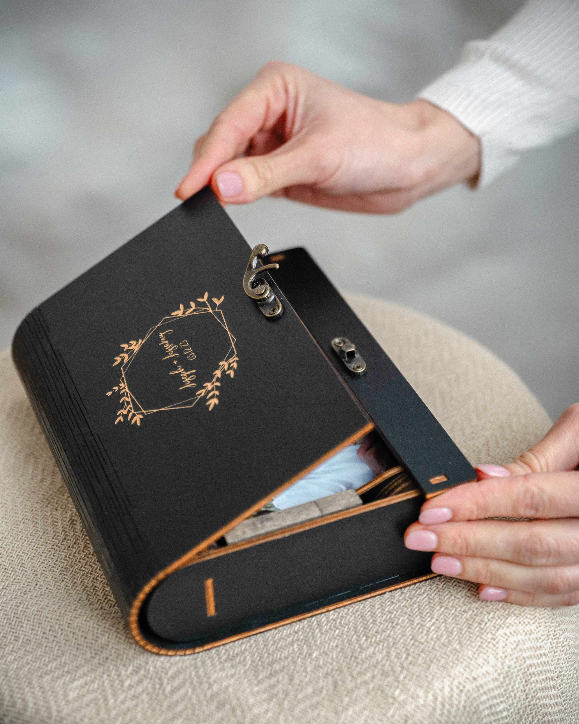 Hands opening black wooden photo box on linen surface, premium client reveal unboxing moment