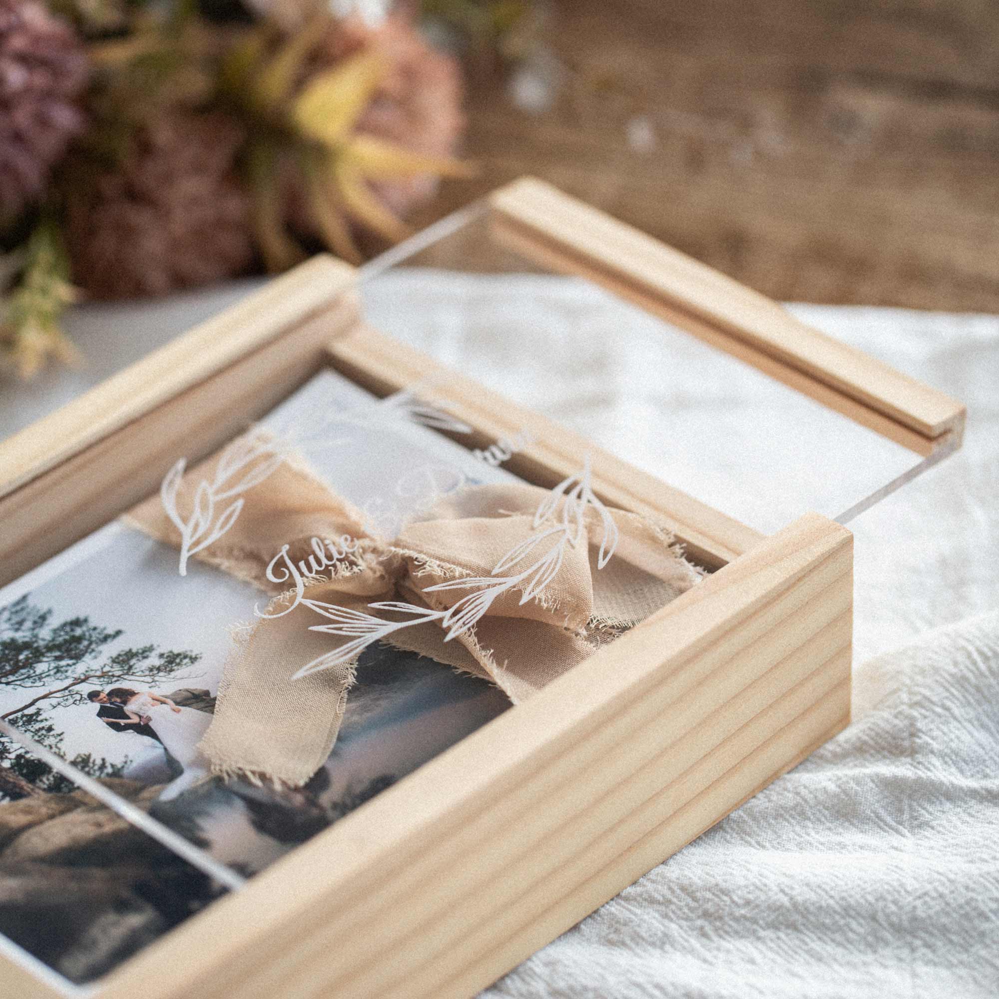 Close-up of wooden box with engraved acrylic lid and linen ribbon bow on top.