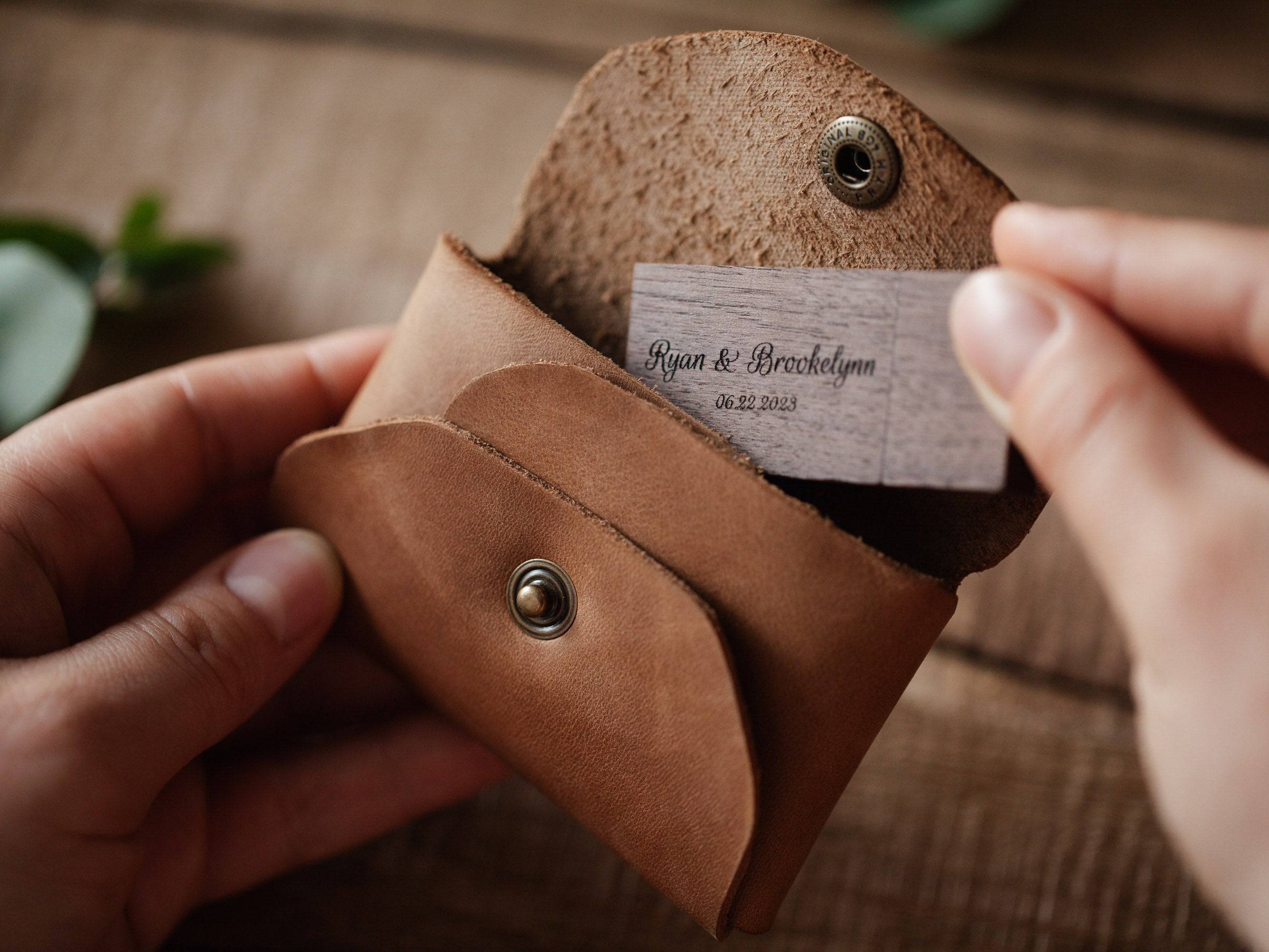 Hands inserting engraved wooden USB flash drive into cognac leather USB envelope