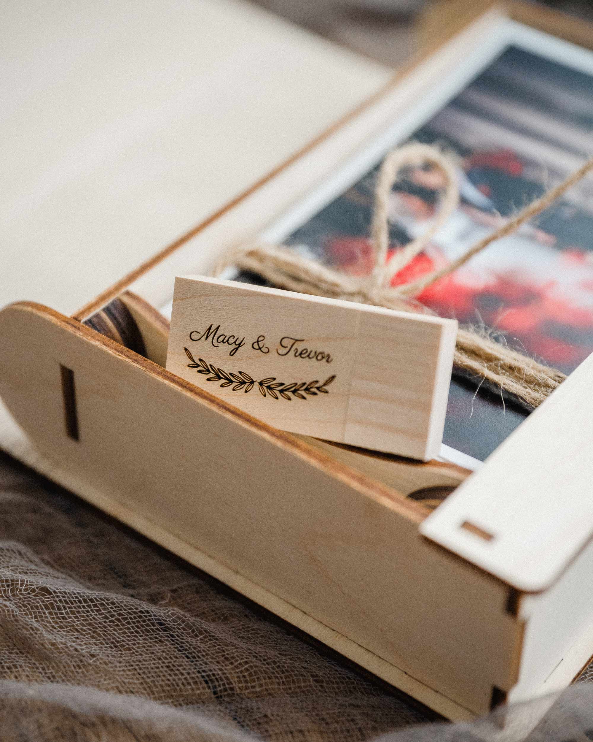 Open maple photo box with prints and a personalized wooden USB in the compartment