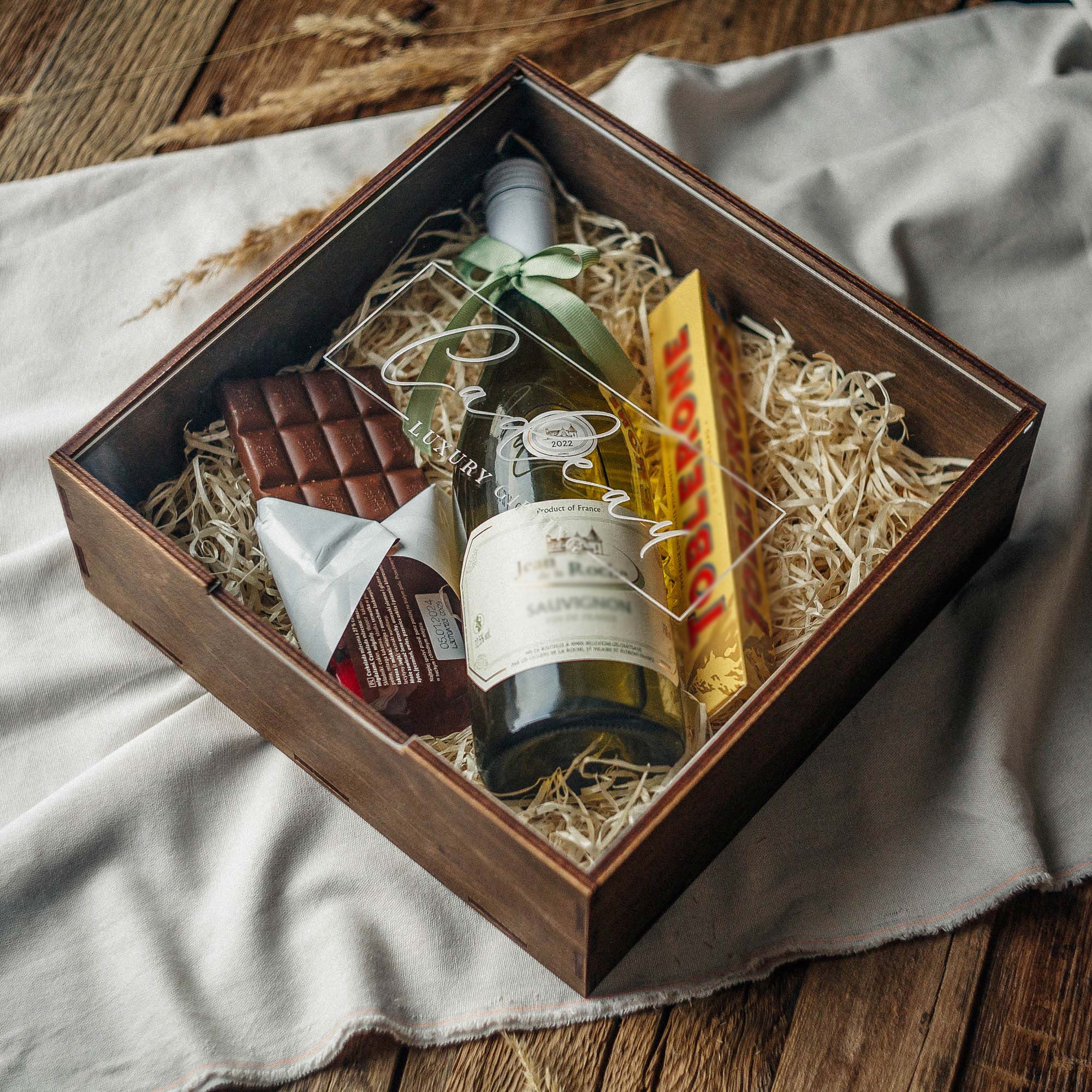 Personalized walnut gift box with acrylic lid holding wine, sweets, and natural filler