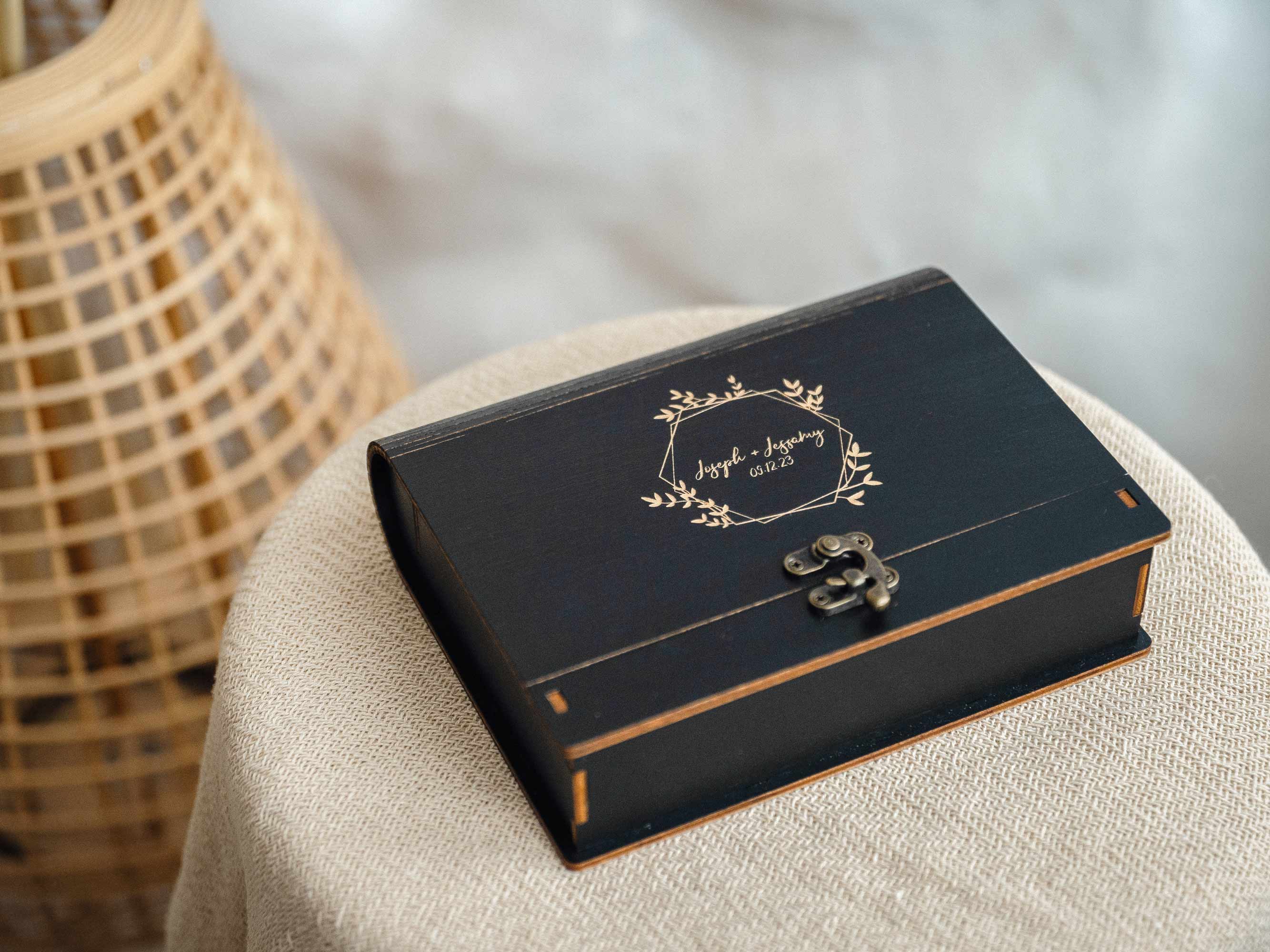 Black wooden photo box with engraved lid on linen ottoman, closed, premium photography packaging