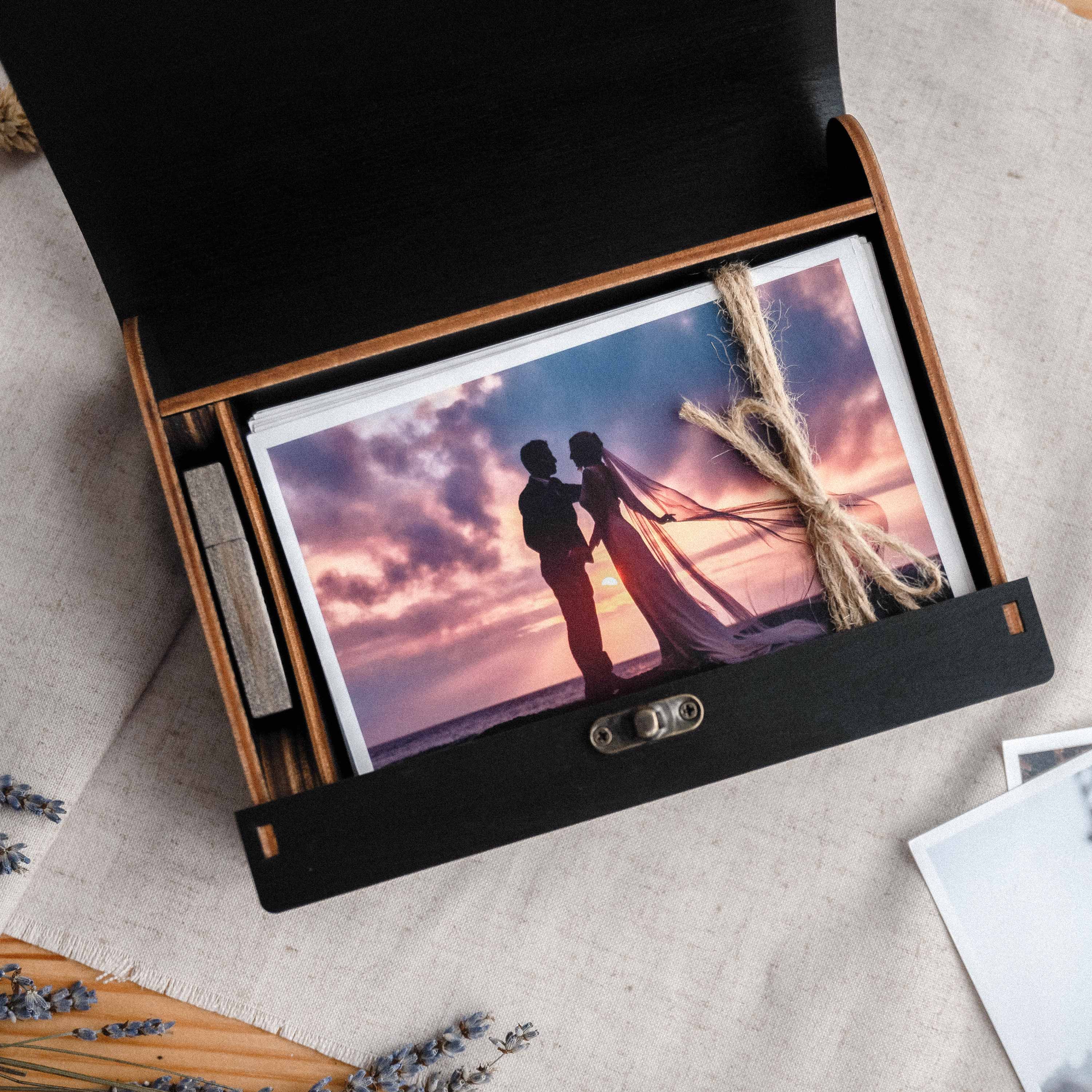 Open black wooden photo box with photo prints inside, premium wedding client presentation box
