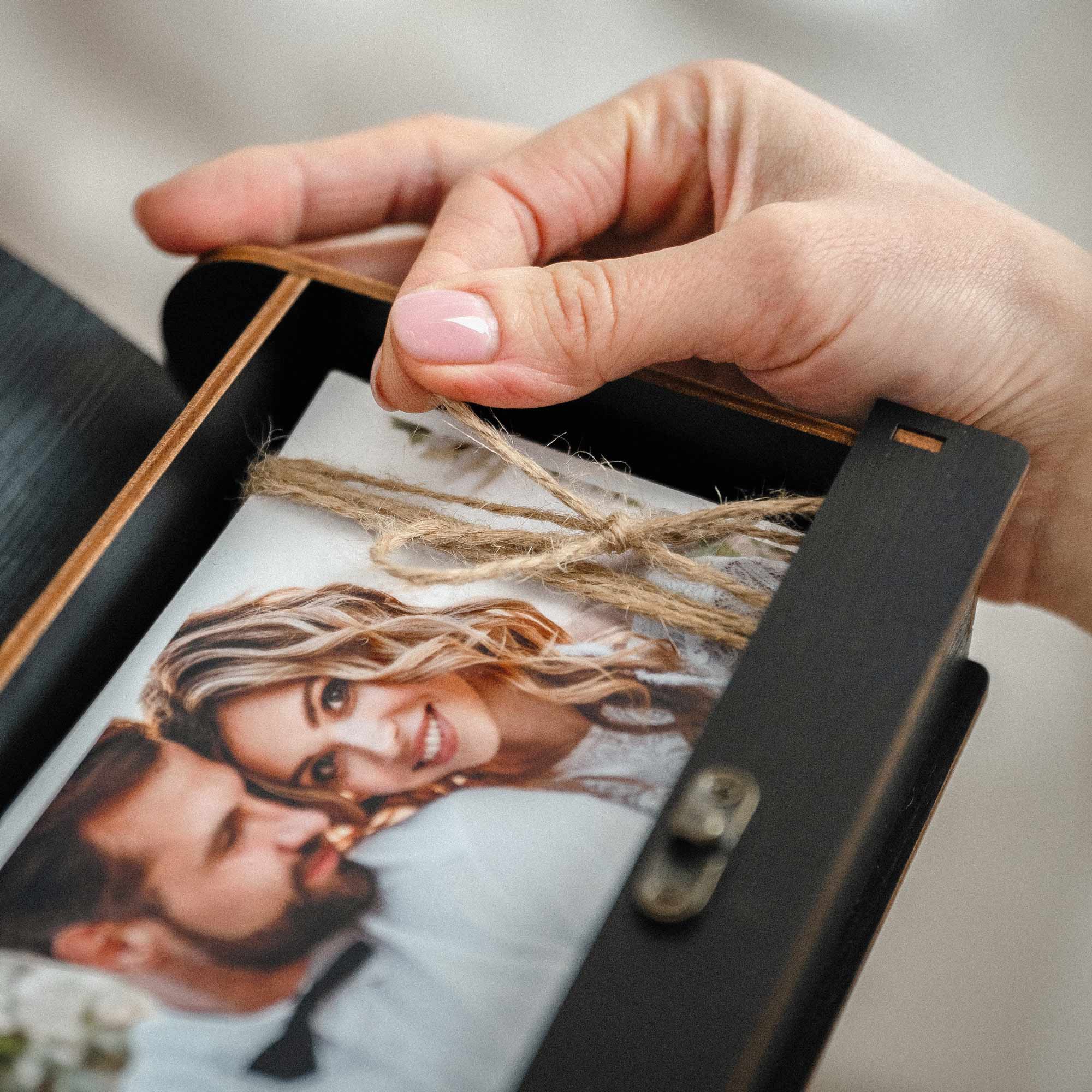Close-up of photo prints tied with twine inside black wooden photo box, handmade keepsake styling
