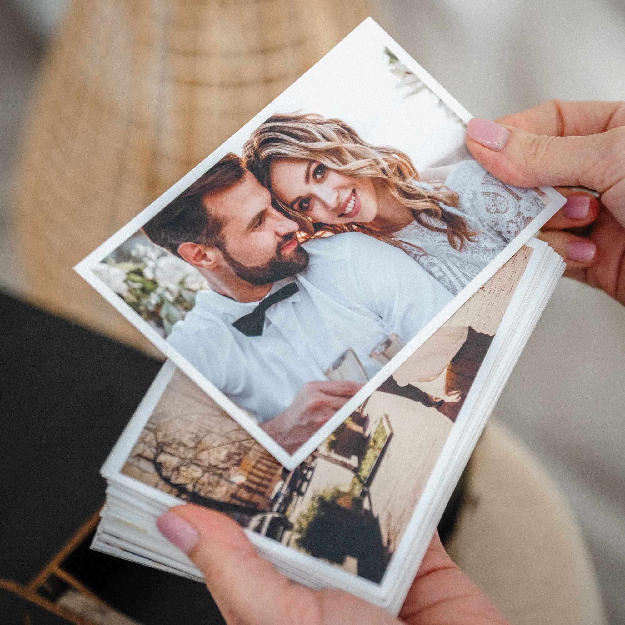 Hands holding a stack of photo prints above open black wooden photo box, wedding keepsake packaging