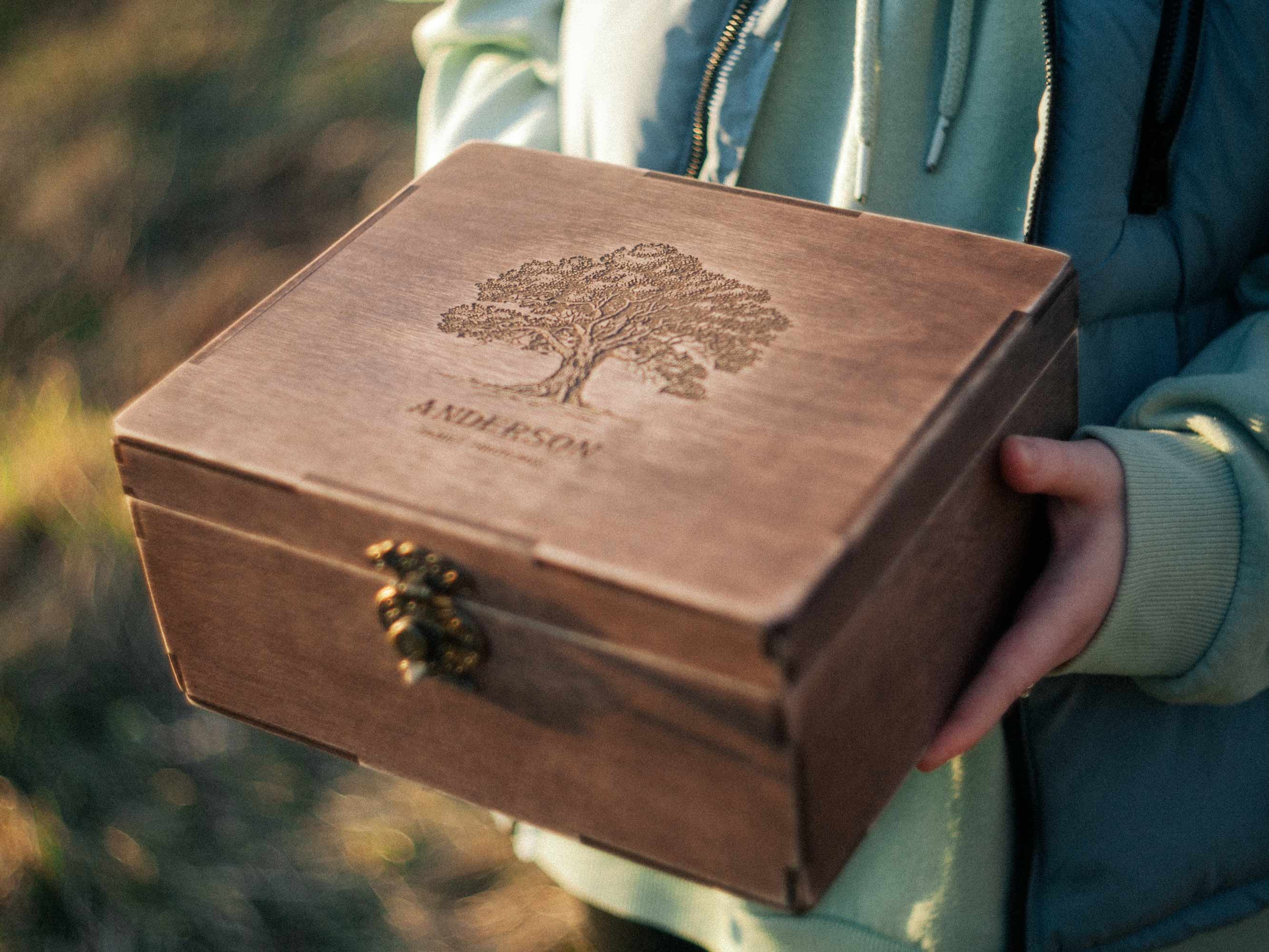 Person holding personalized wooden family photo box with engraved tree design outdoors