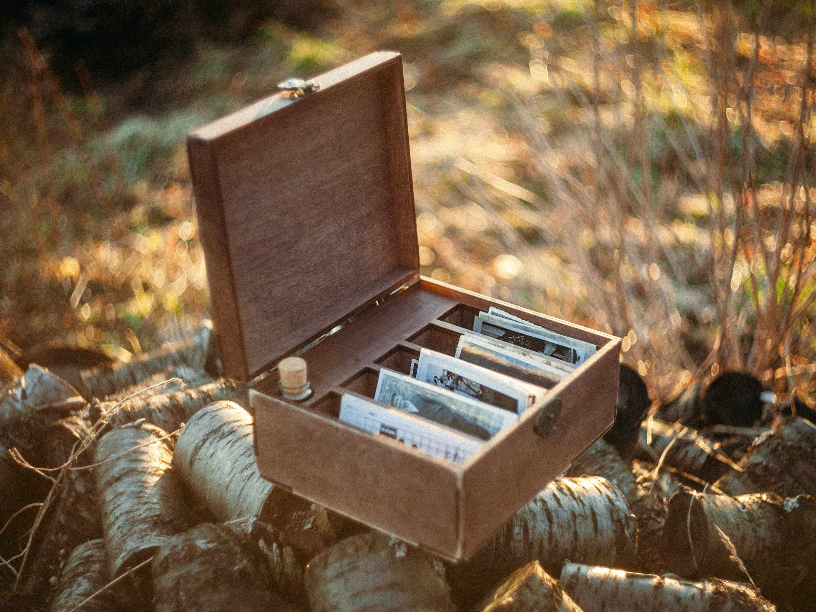 Open wooden family photo box with five sections and glass bottle USB displayed outdoors