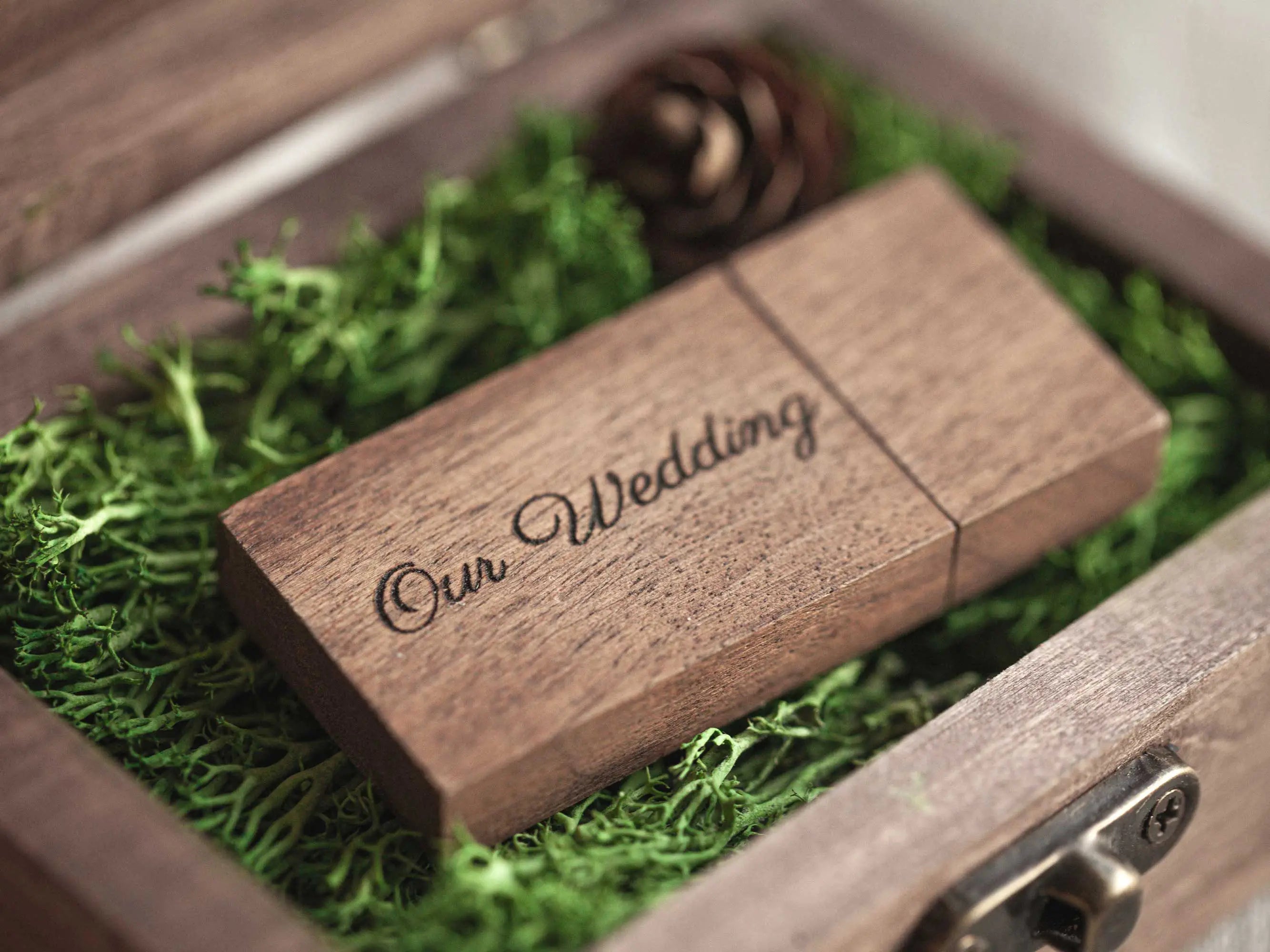 Close-up of the engraved wooden USB drive resting on moss inside the box.