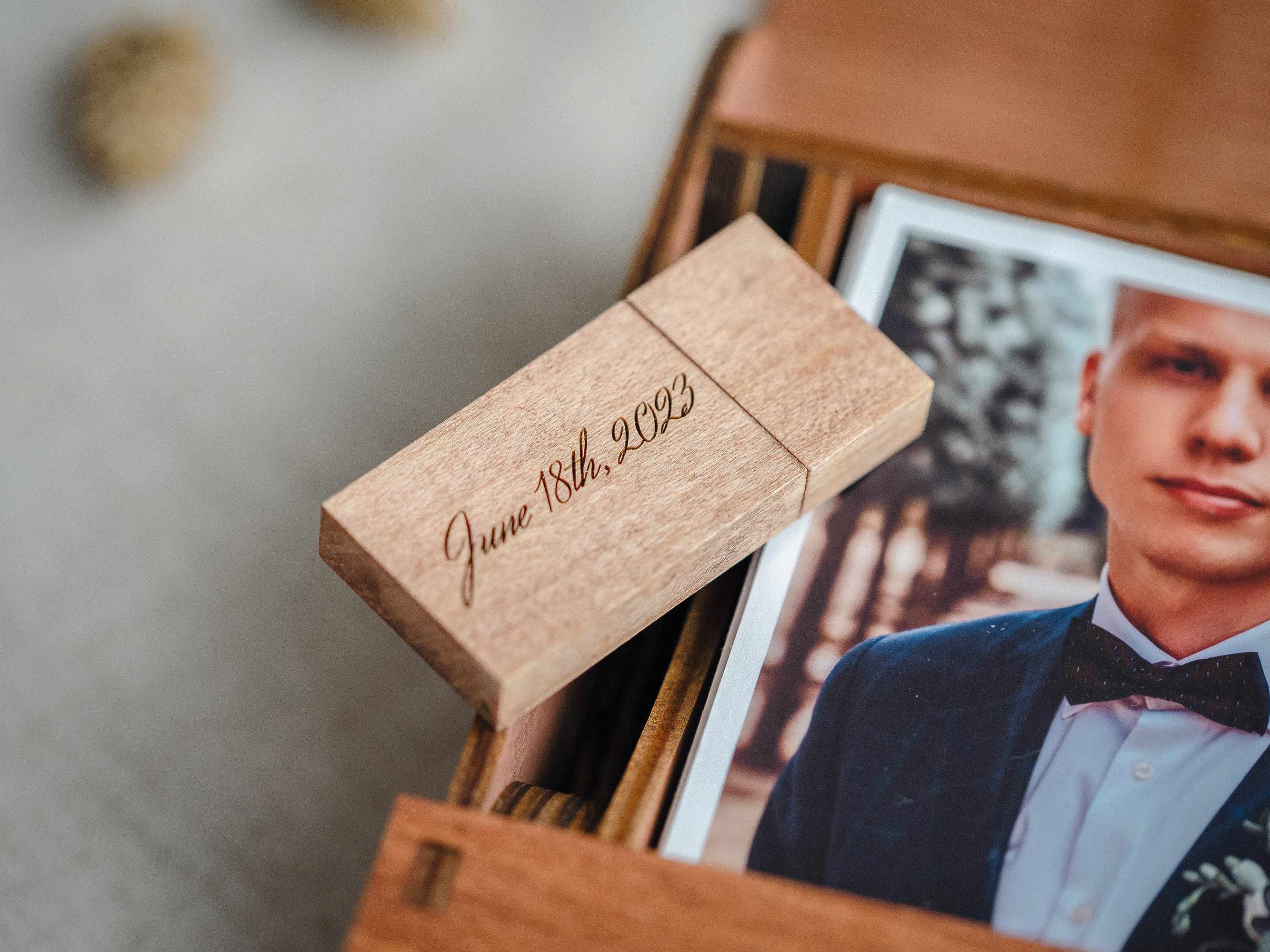 Engraved wooden USB flash drive on wedding photos beside teak photo box