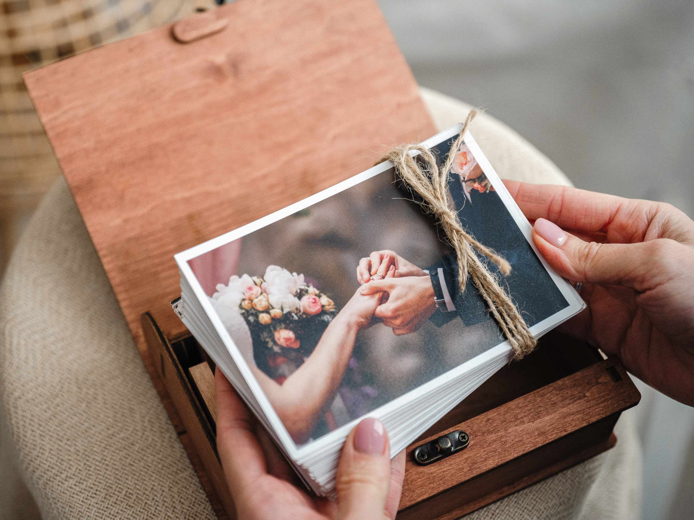 Hands holding wedding prints above open teak photo box, premium client unboxing moment