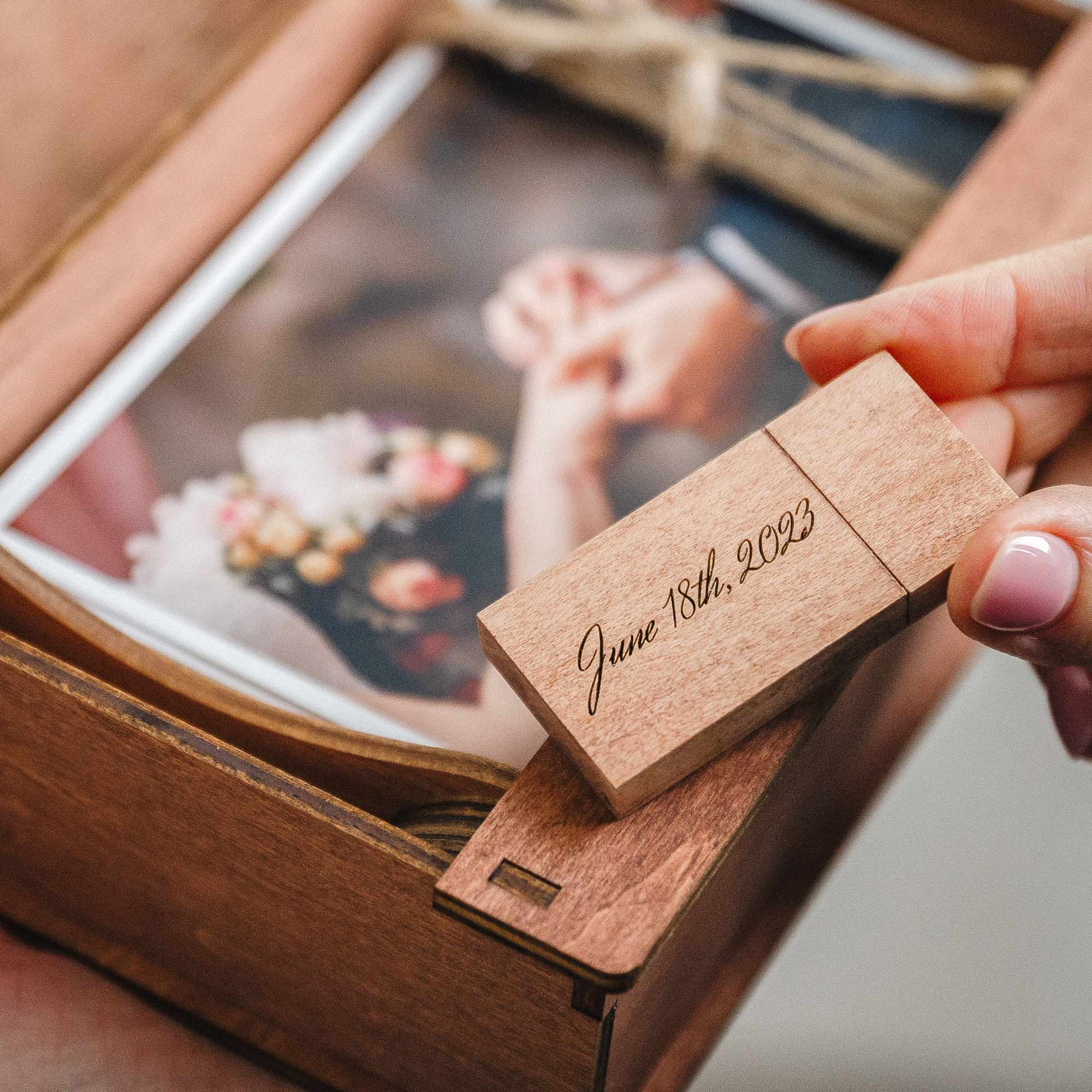 Hand holding engraved wooden USB flash drive above teak photo box with prints inside