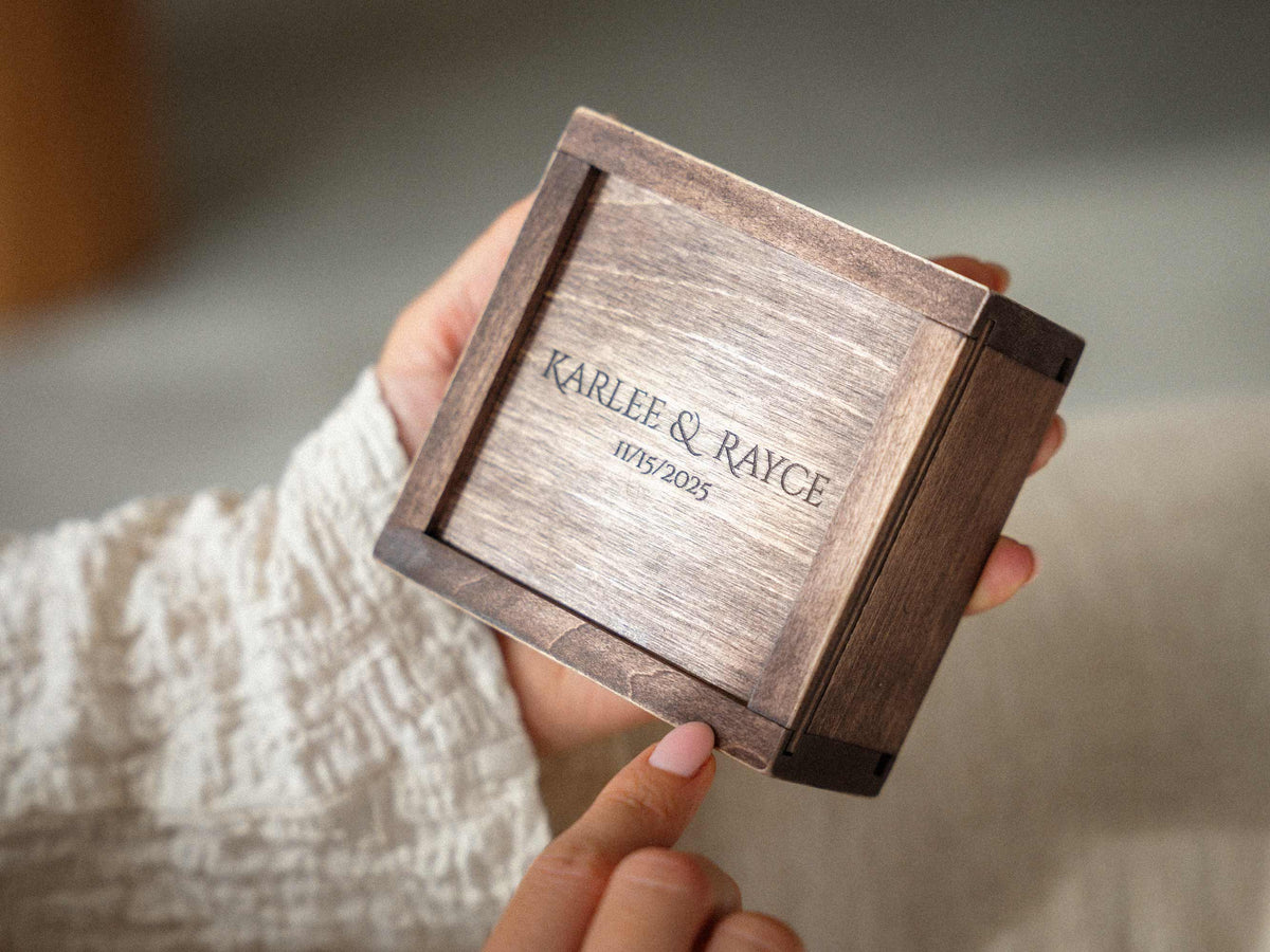 Small personalized wooden USB box with engraved wedding names on the sliding lid, held in hands.