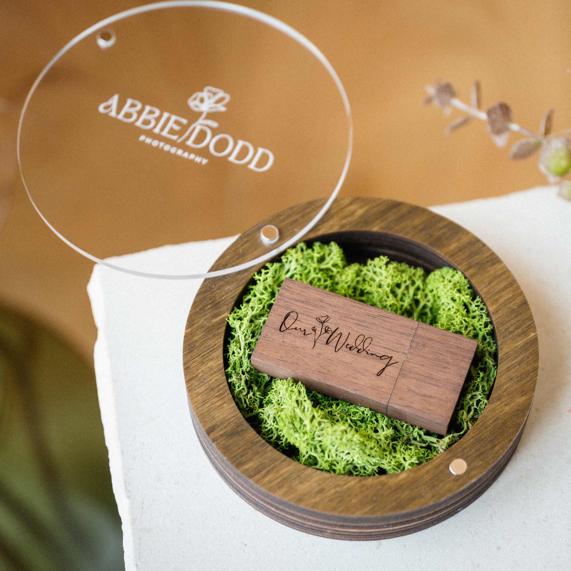 Personalized walnut USB box with open acrylic lid and wooden flash drive on green moss