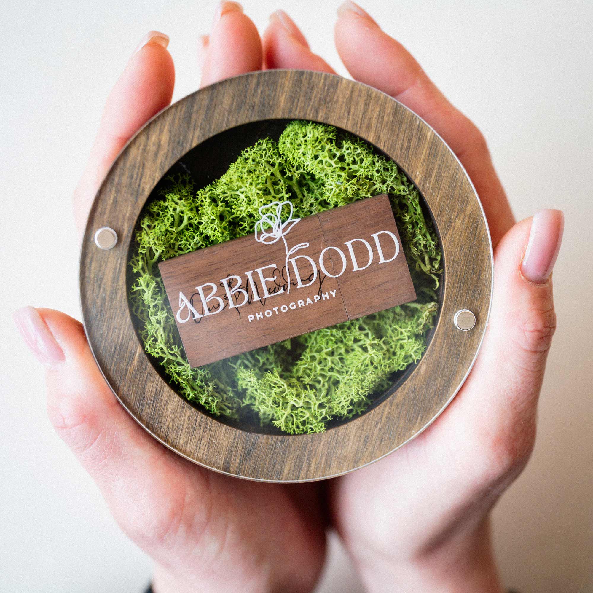 Top view of personalized walnut USB box with wooden flash drive on green moss in hands