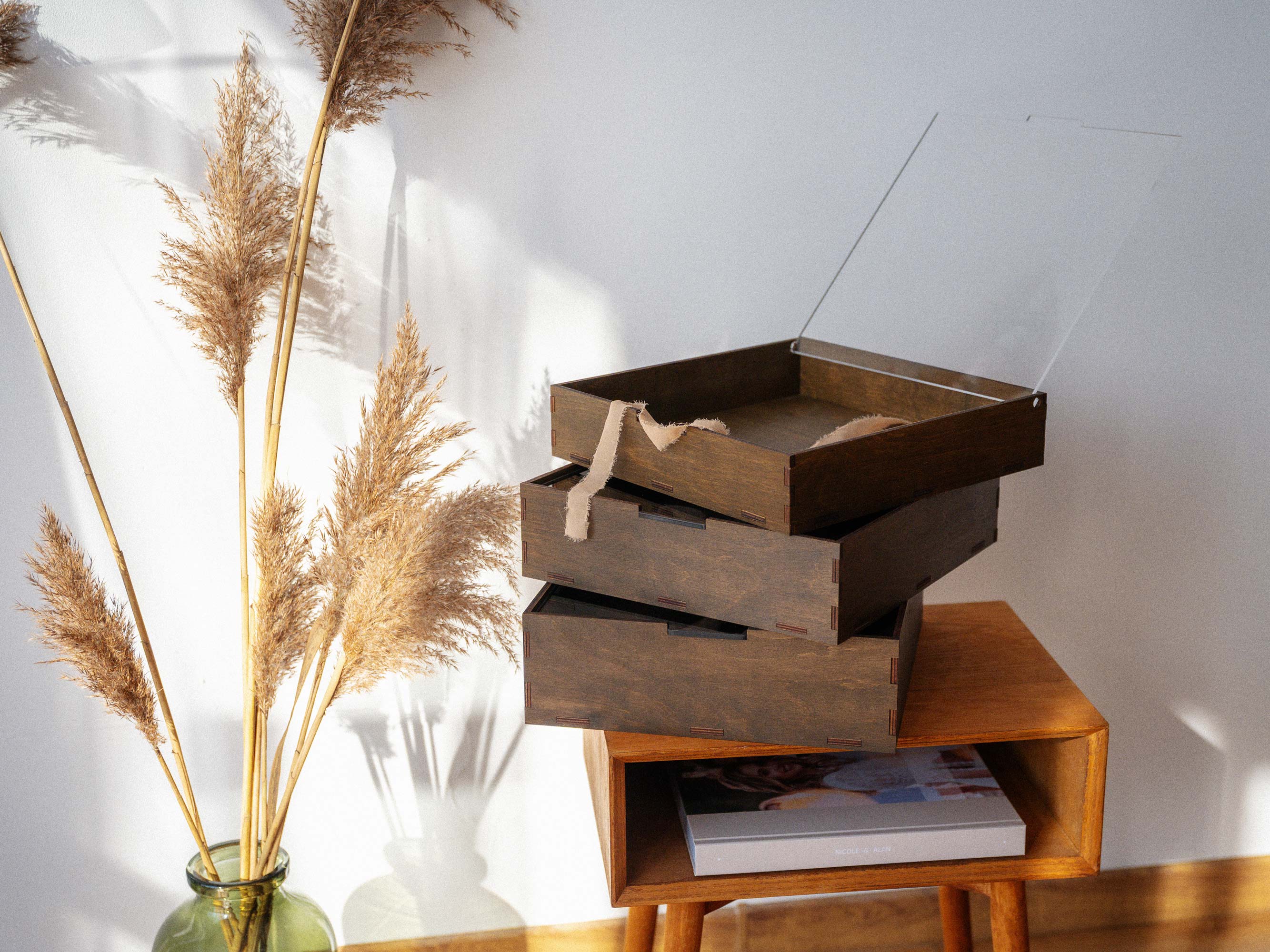 Walnut gift boxes with acrylic lids stacked near pampas grass decor