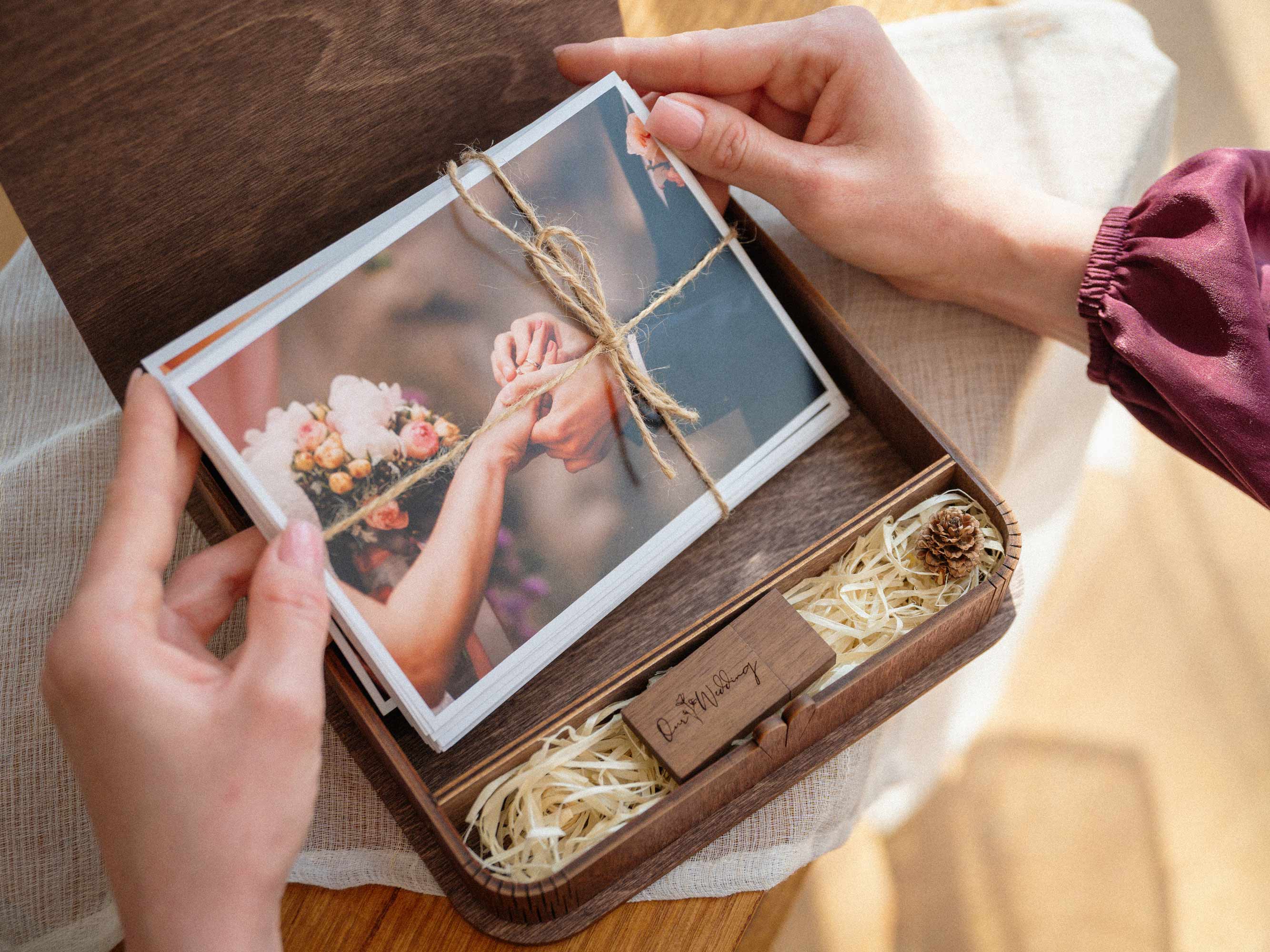 Hands holding wedding prints inside walnut wooden photo box with USB