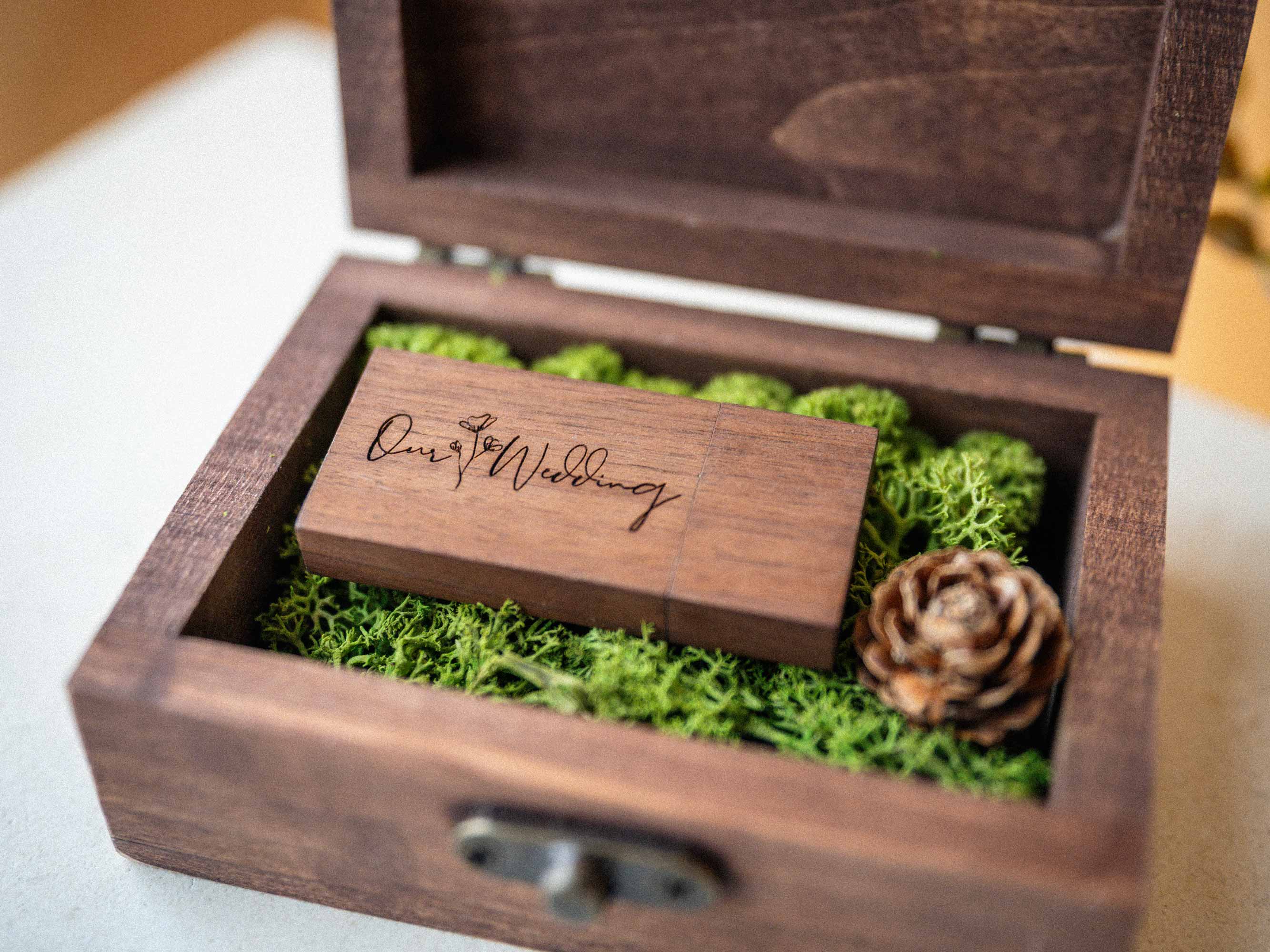 Open walnut wooden USB box with engraved flash drive, moss and pine cone