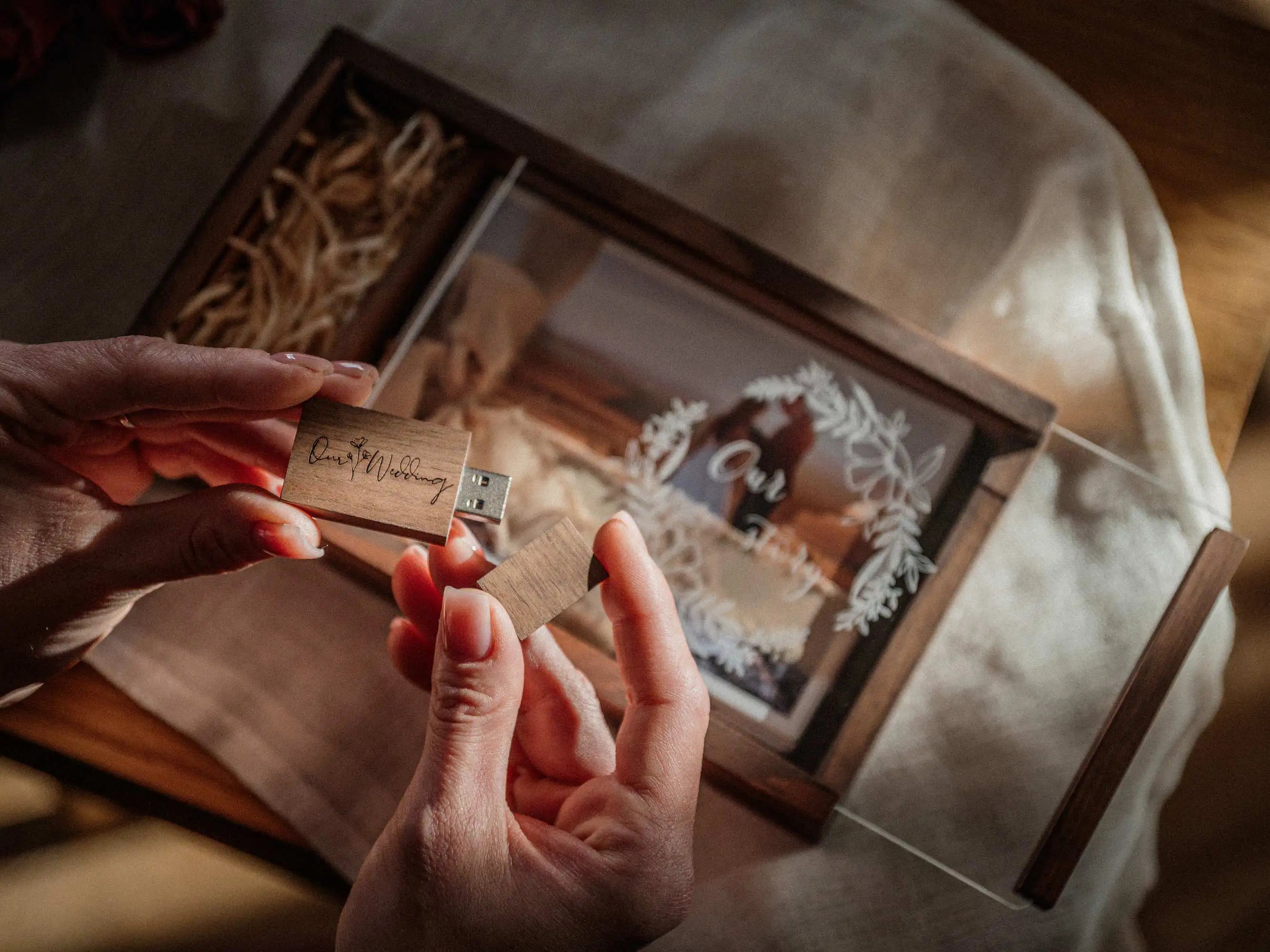 Hands arranging ribbon and wooden USB inside wedding photo box with printed photo