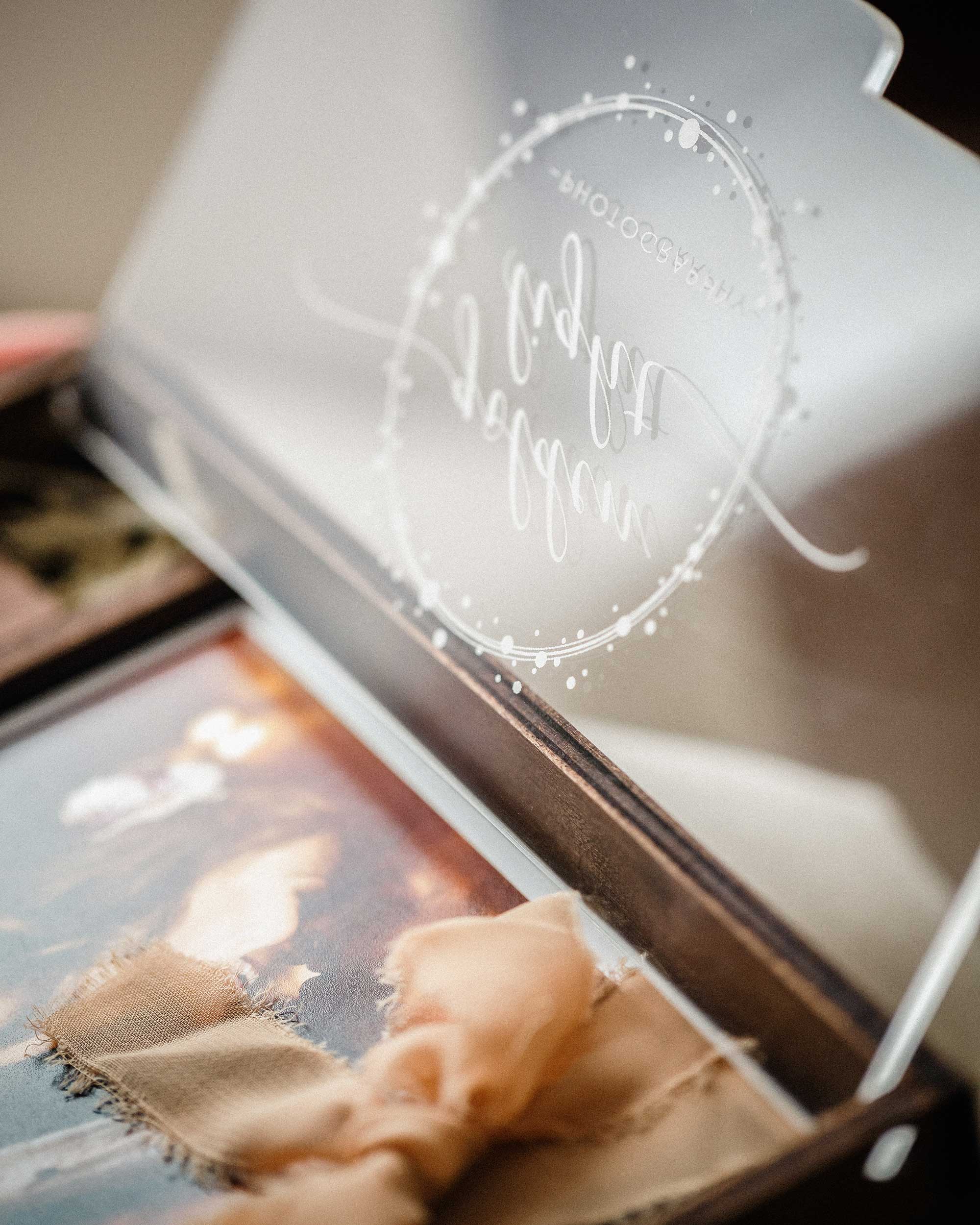 Closed wooden wedding photo box with personalized acrylic lid on neutral fabric background