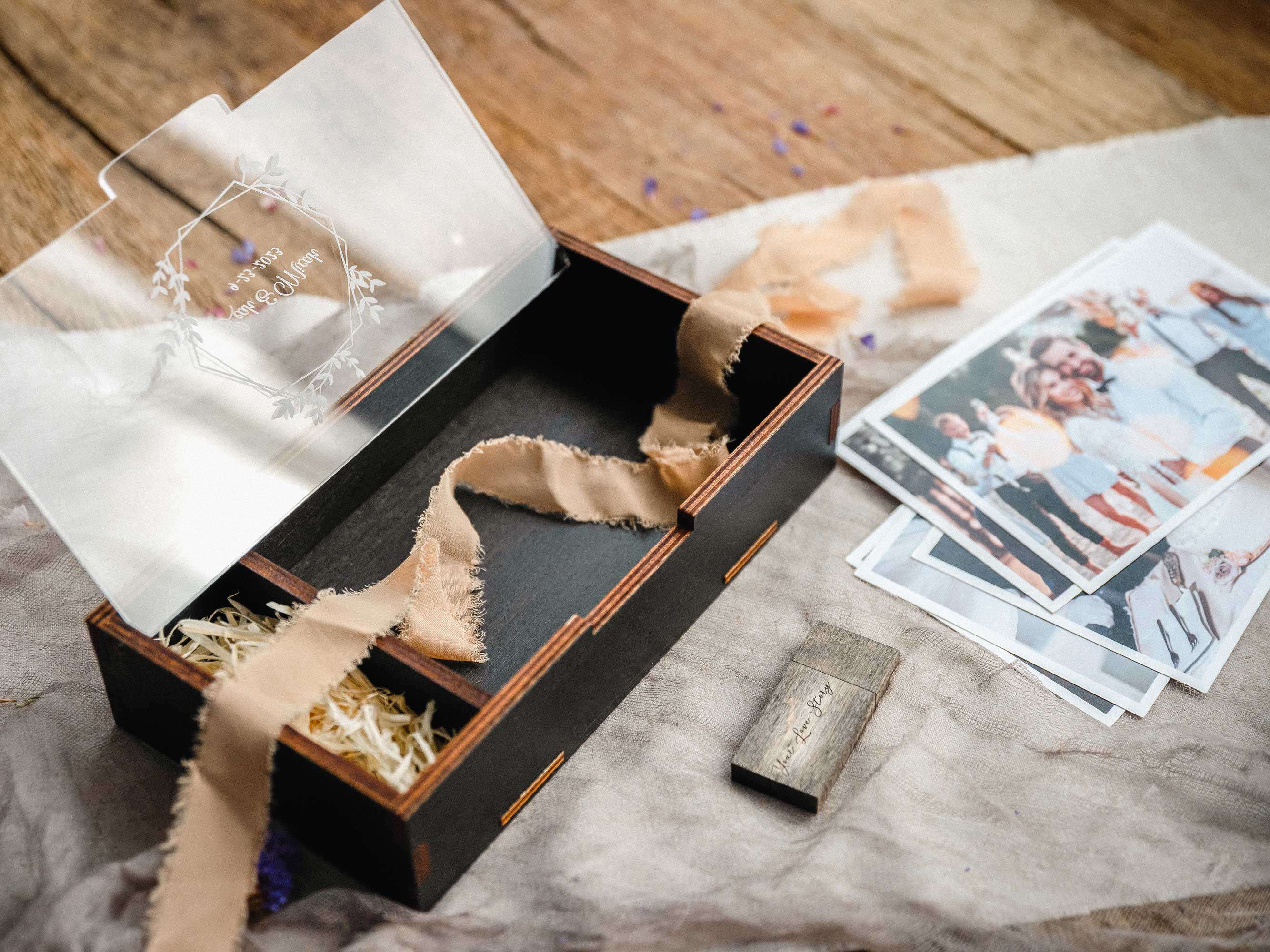 Open black wedding photo box with personalized acrylic lid, ribbon, and loose prints