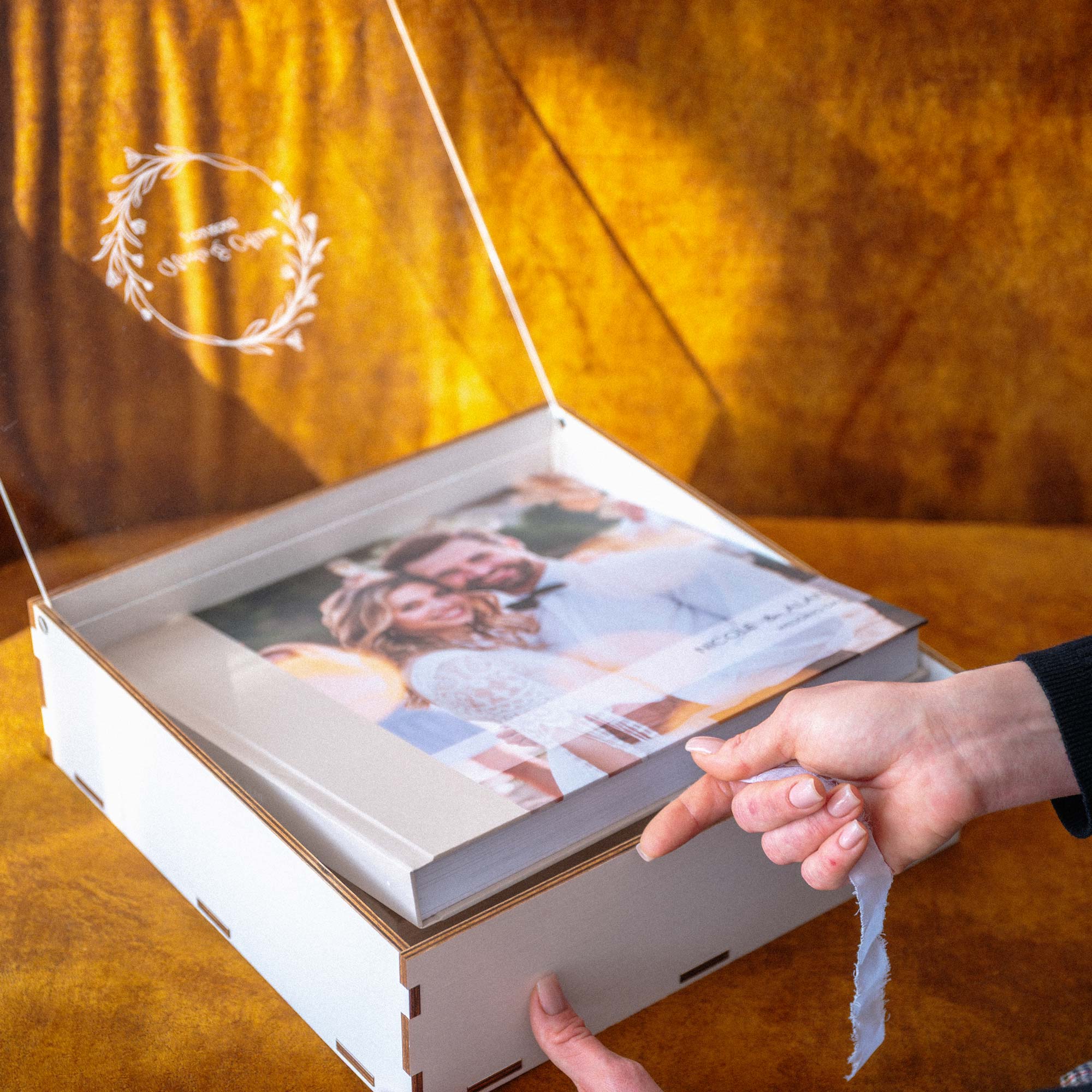 Hands pulling ribbon from 10x10 photo album inside personalized white wooden box