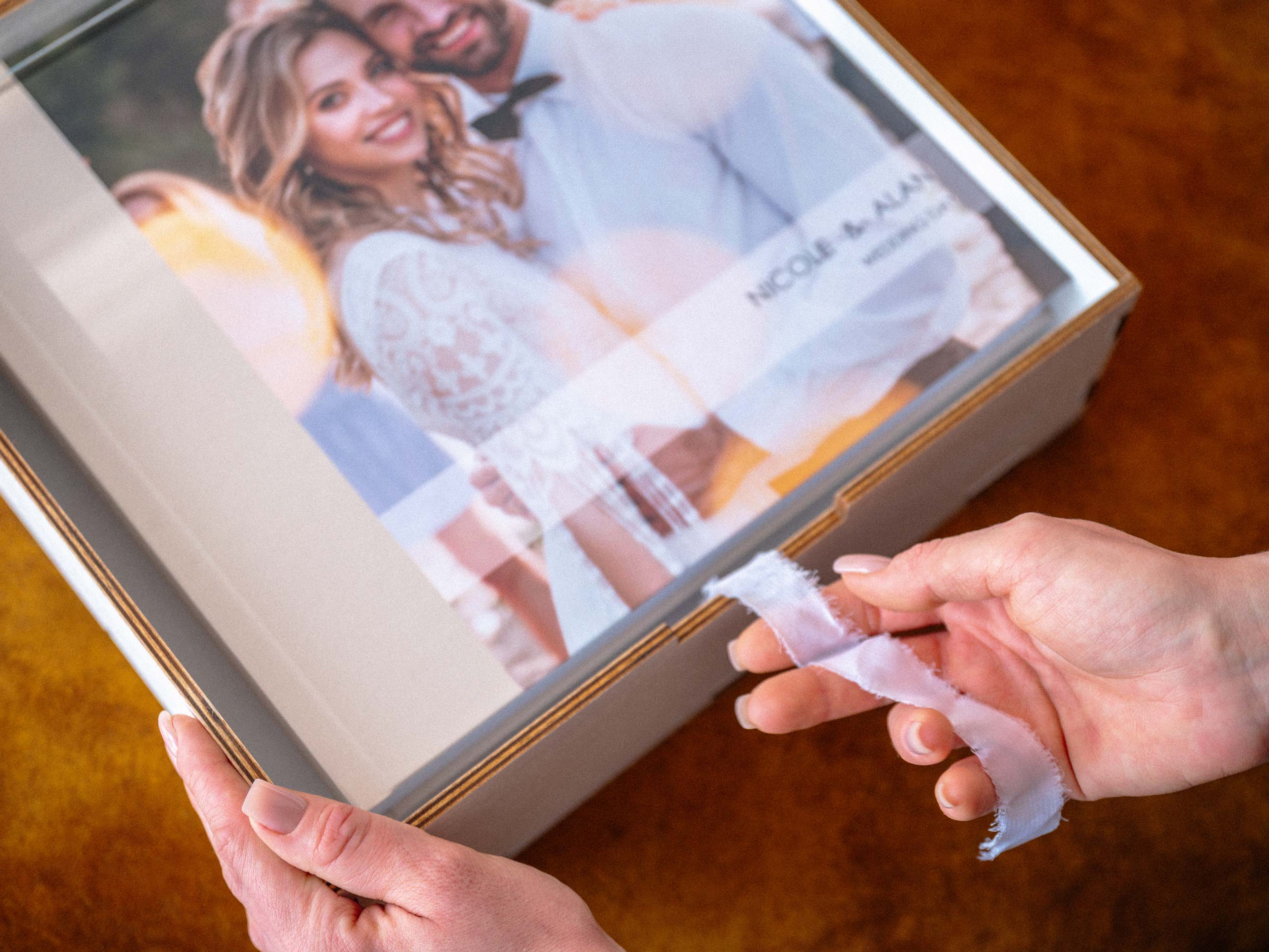 Hands pulling ribbon from 12x12 wedding album inside white acrylic lid box