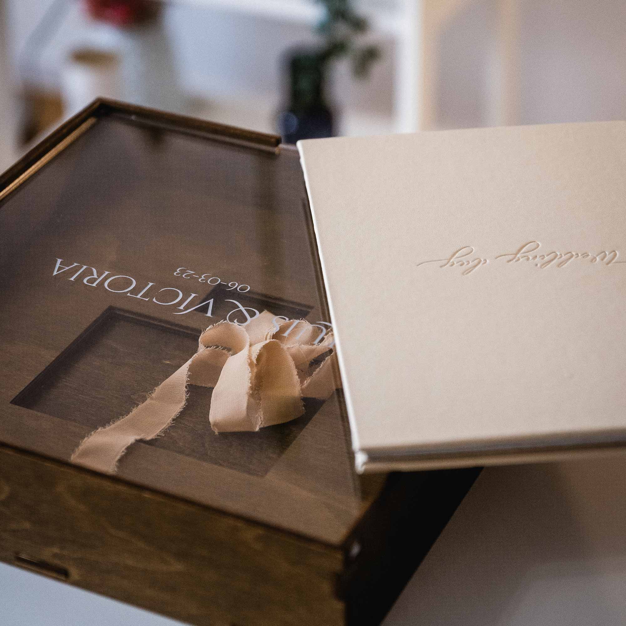 Wooden wedding album box with acrylic lid next to square photo album on table