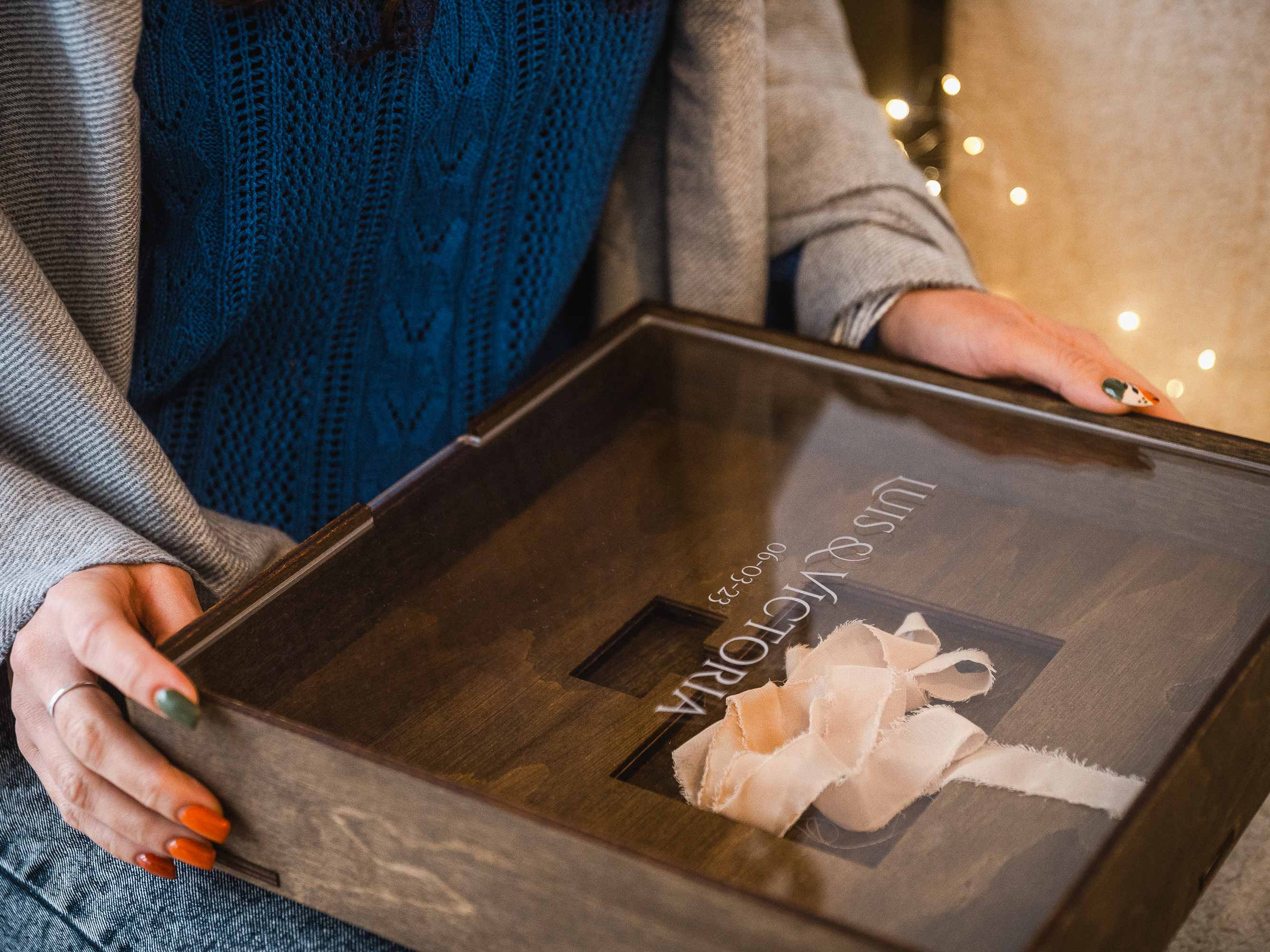 Person holding wooden wedding album box with acrylic lid and ribbon inside