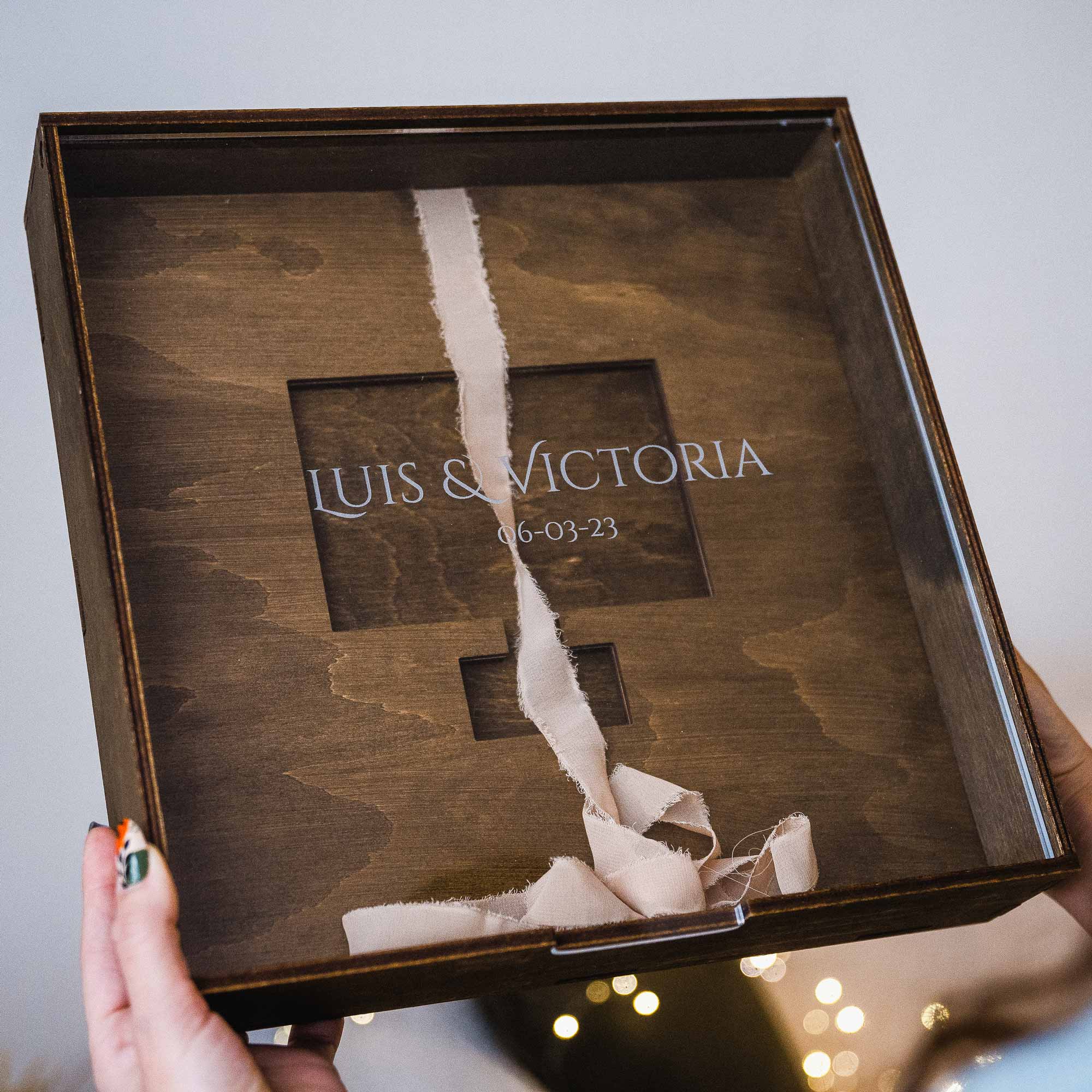Person holding wooden wedding album box with acrylic lid in hands near window