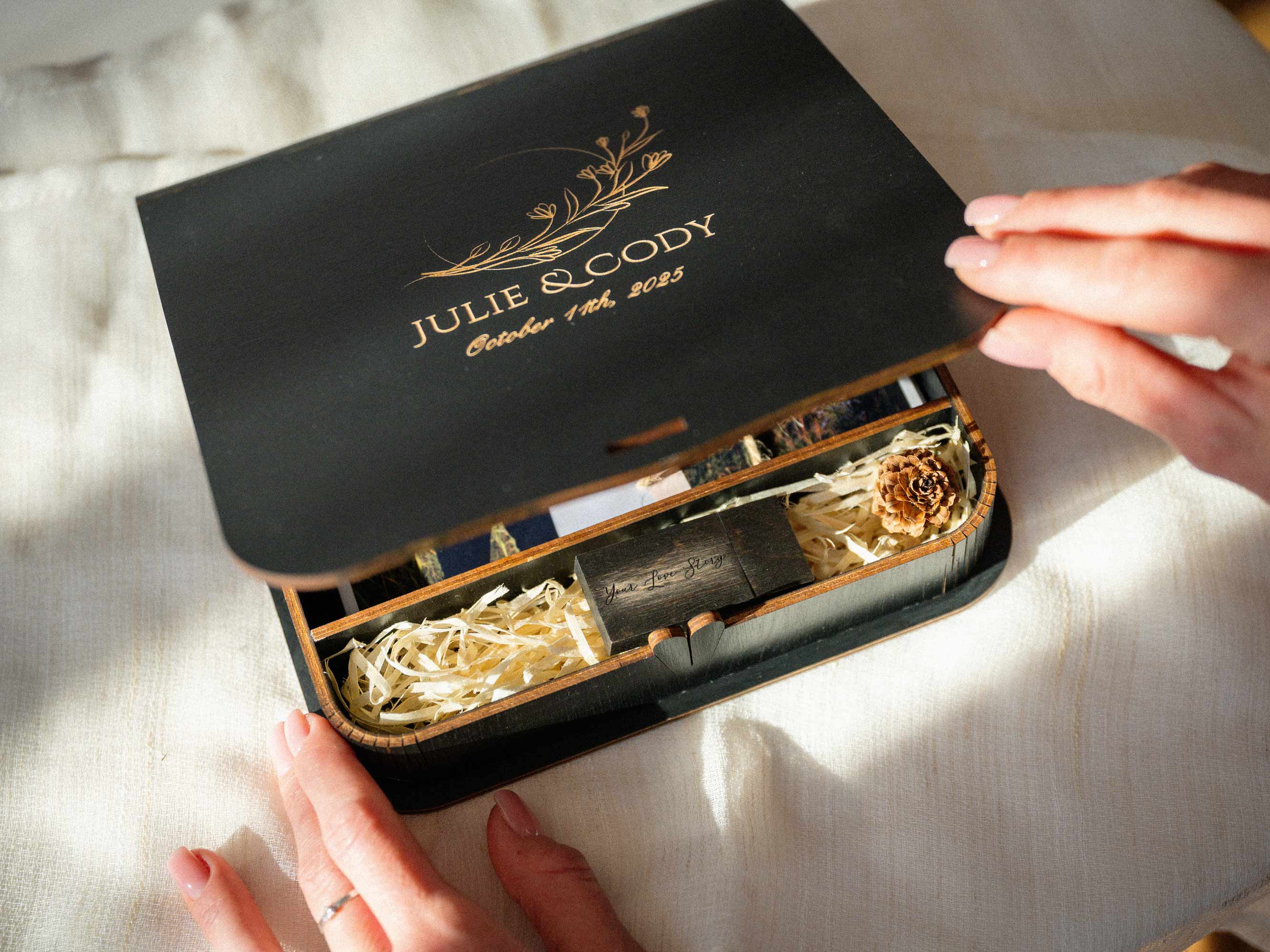 Hands opening black engraved wooden photo box with wedding prints and USB