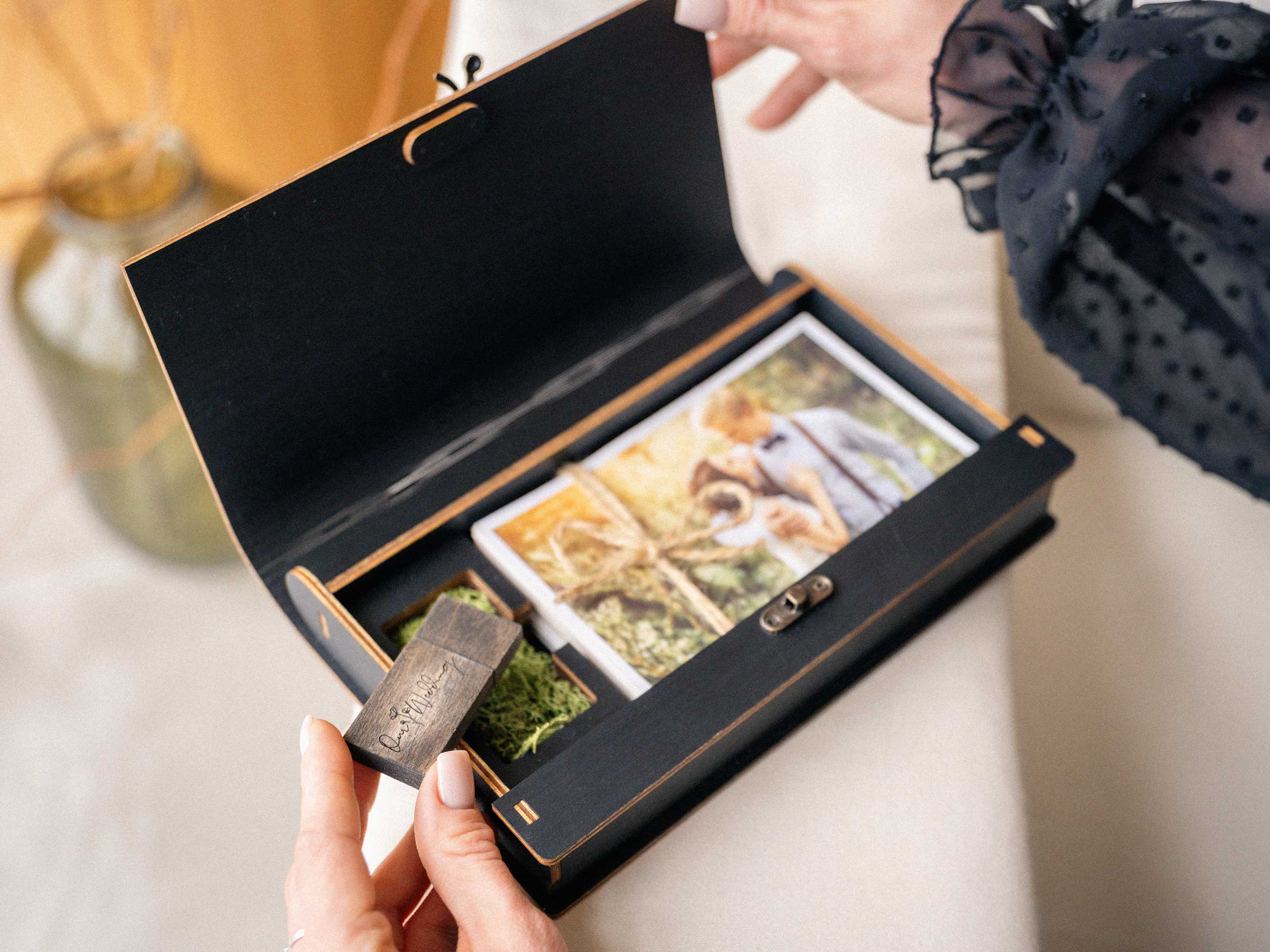 Open black photo box with USB flash drive and photos tied with linen cord