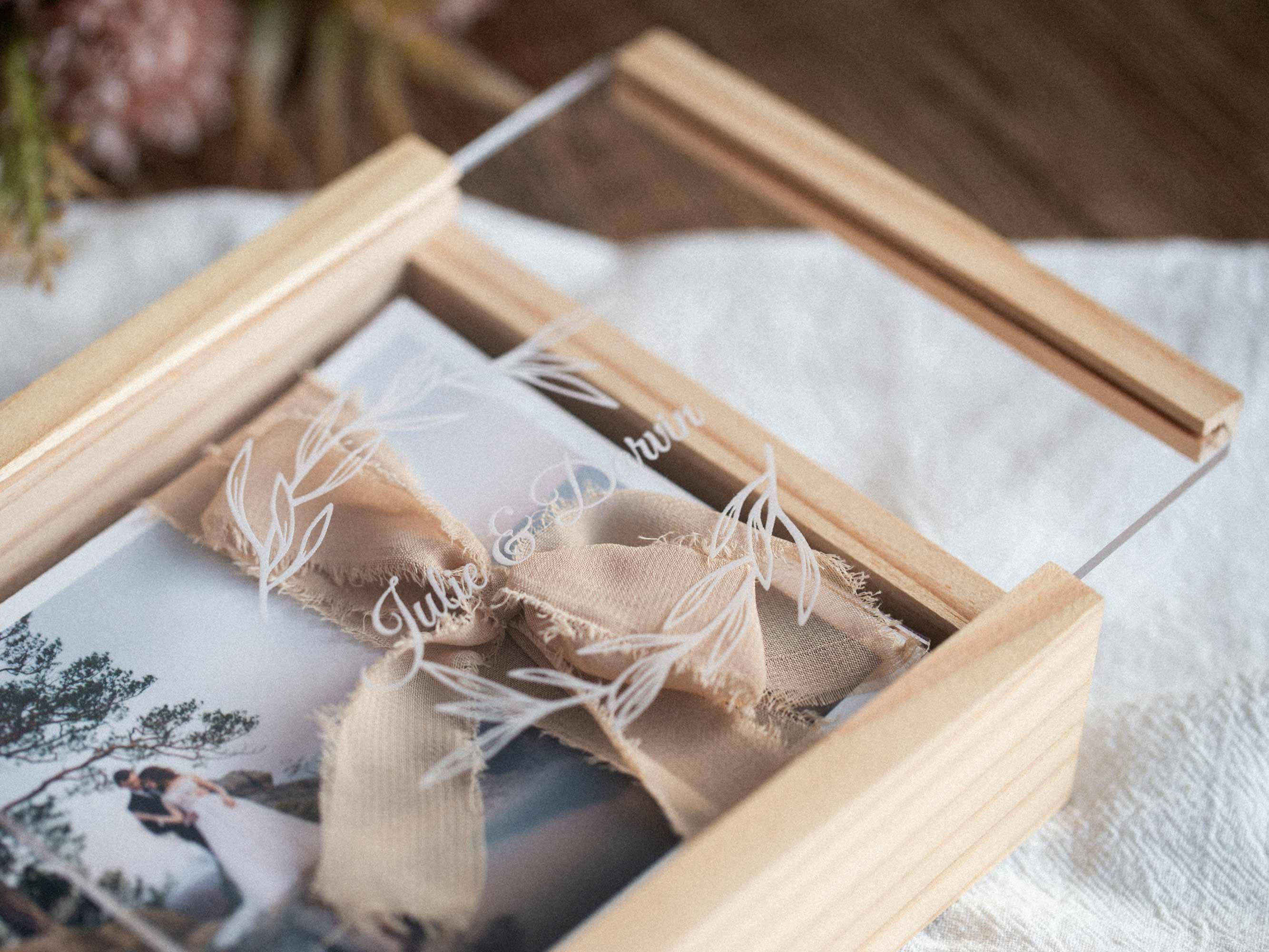 Close-up corner view of maple wooden photo box with acrylic lid and ribbon bow, photo visible under lid.