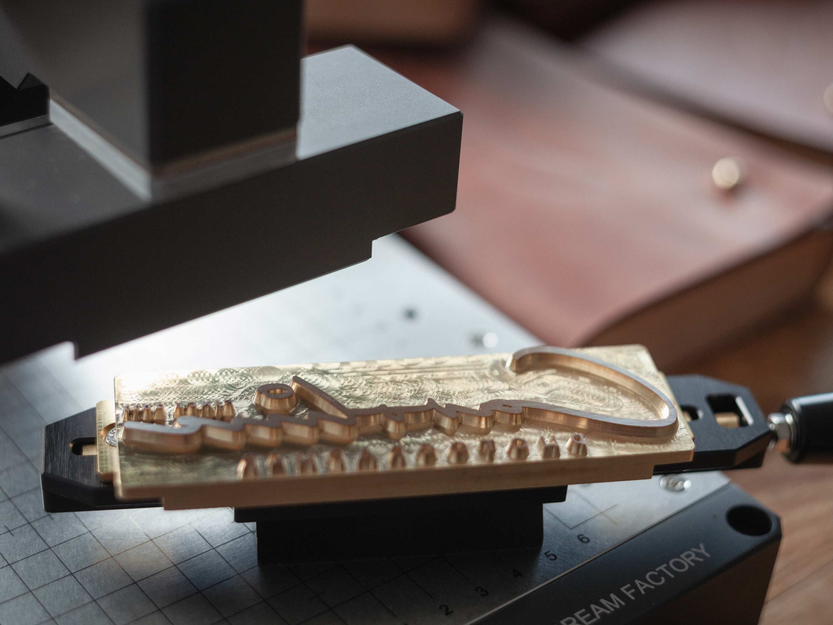 Brass logo stamp and leather envelope positioned under the hot stamping machine head.