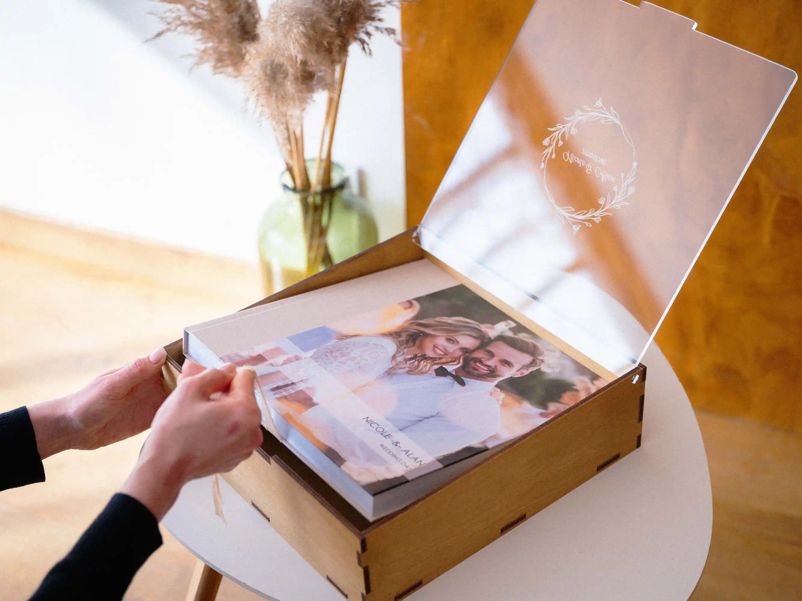 Hand lifting a wedding album from an open Gold Oak album box with acrylic lid
