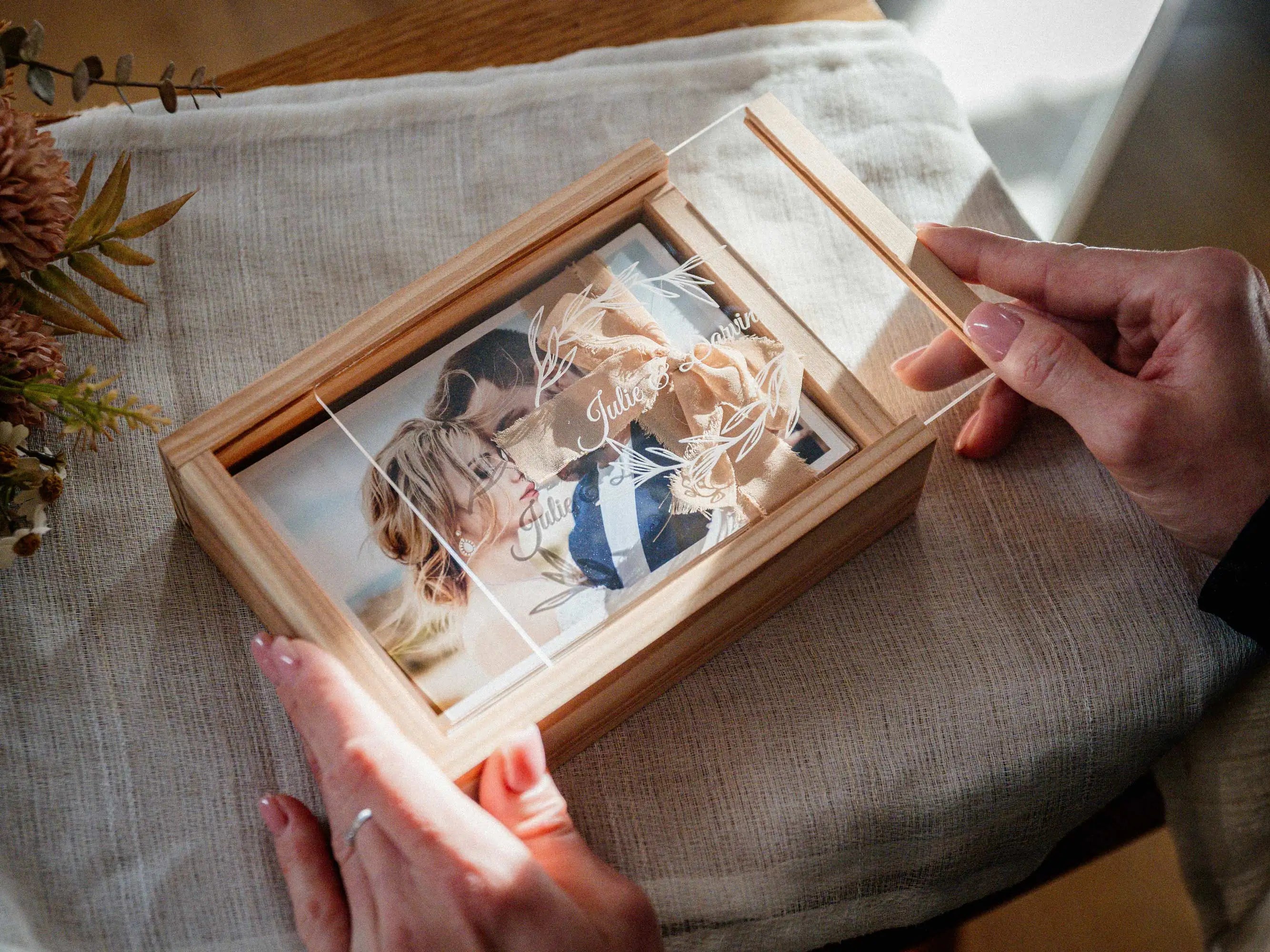 Hands opening maple wooden photo box with personalized acrylic lid and wedding prints