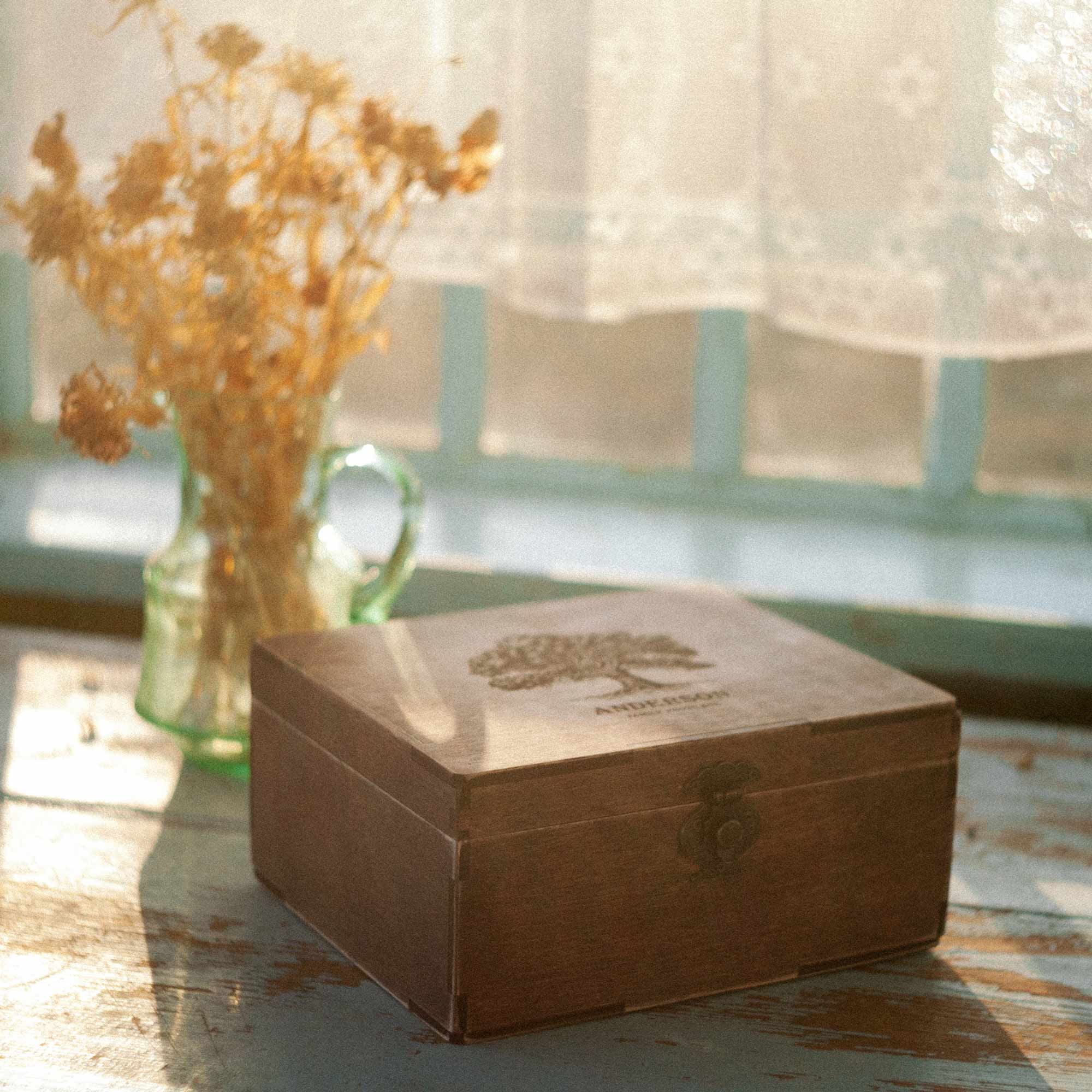 Closed wooden family photo box in warm sunlight near dried flowers