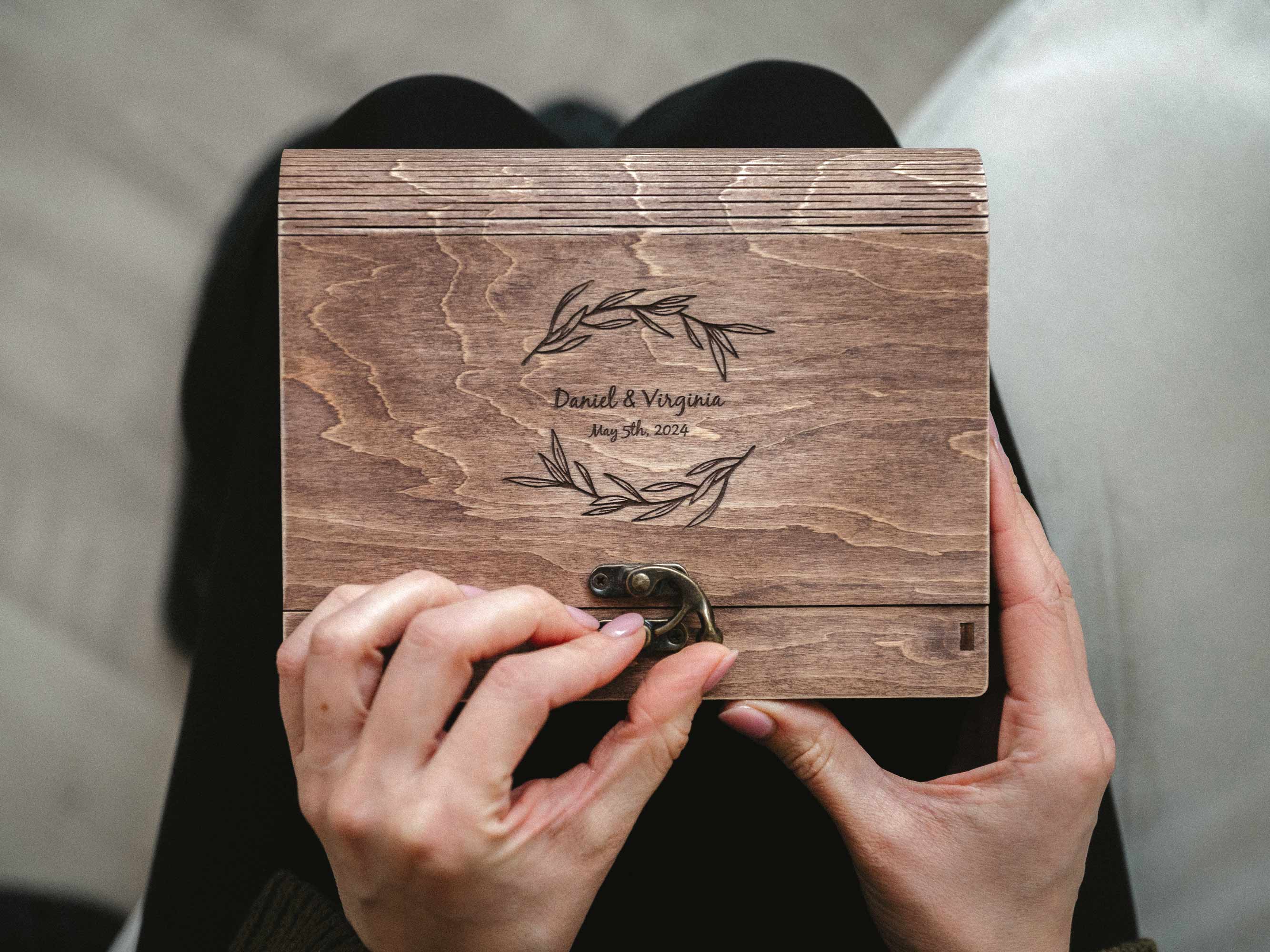 Hands opening personalized vintage walnut wedding photo box with engraved lid and metal hook clasp