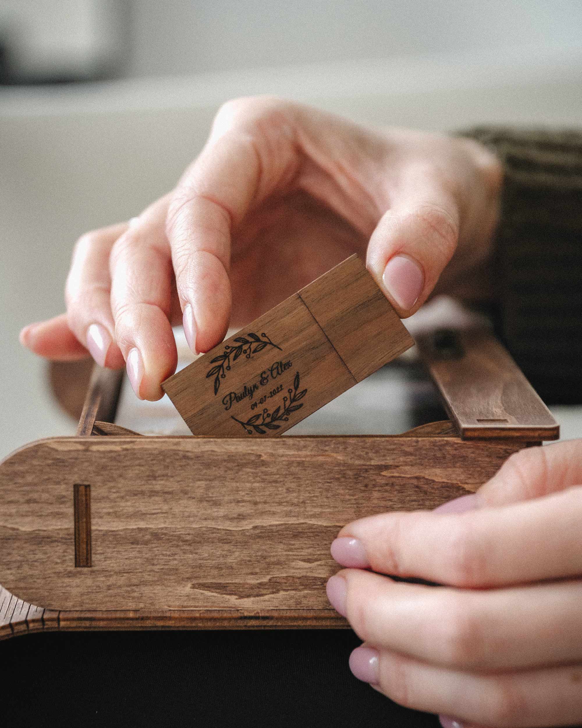 Hand removing wooden USB from compartment in personalized walnut wedding photo box