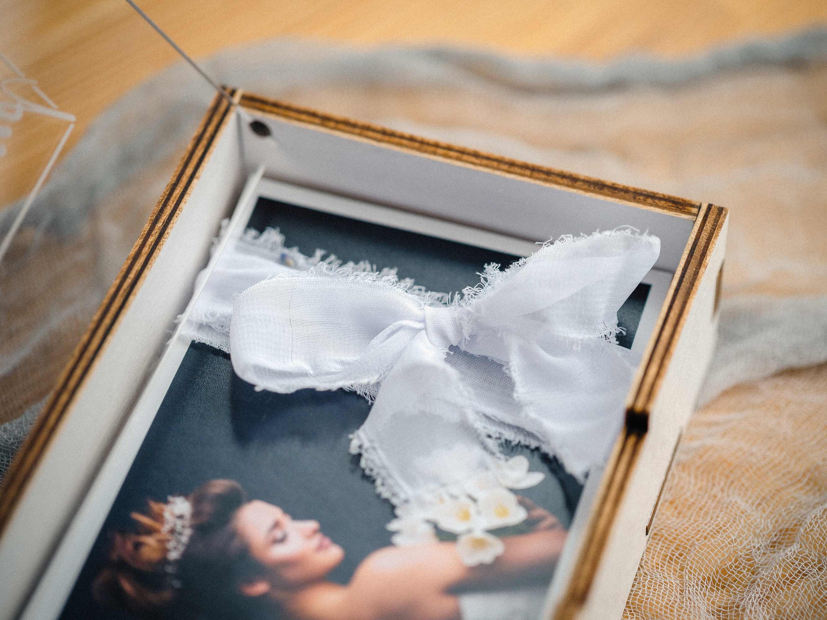 White linen ribbon tied around photo prints inside white wooden box.