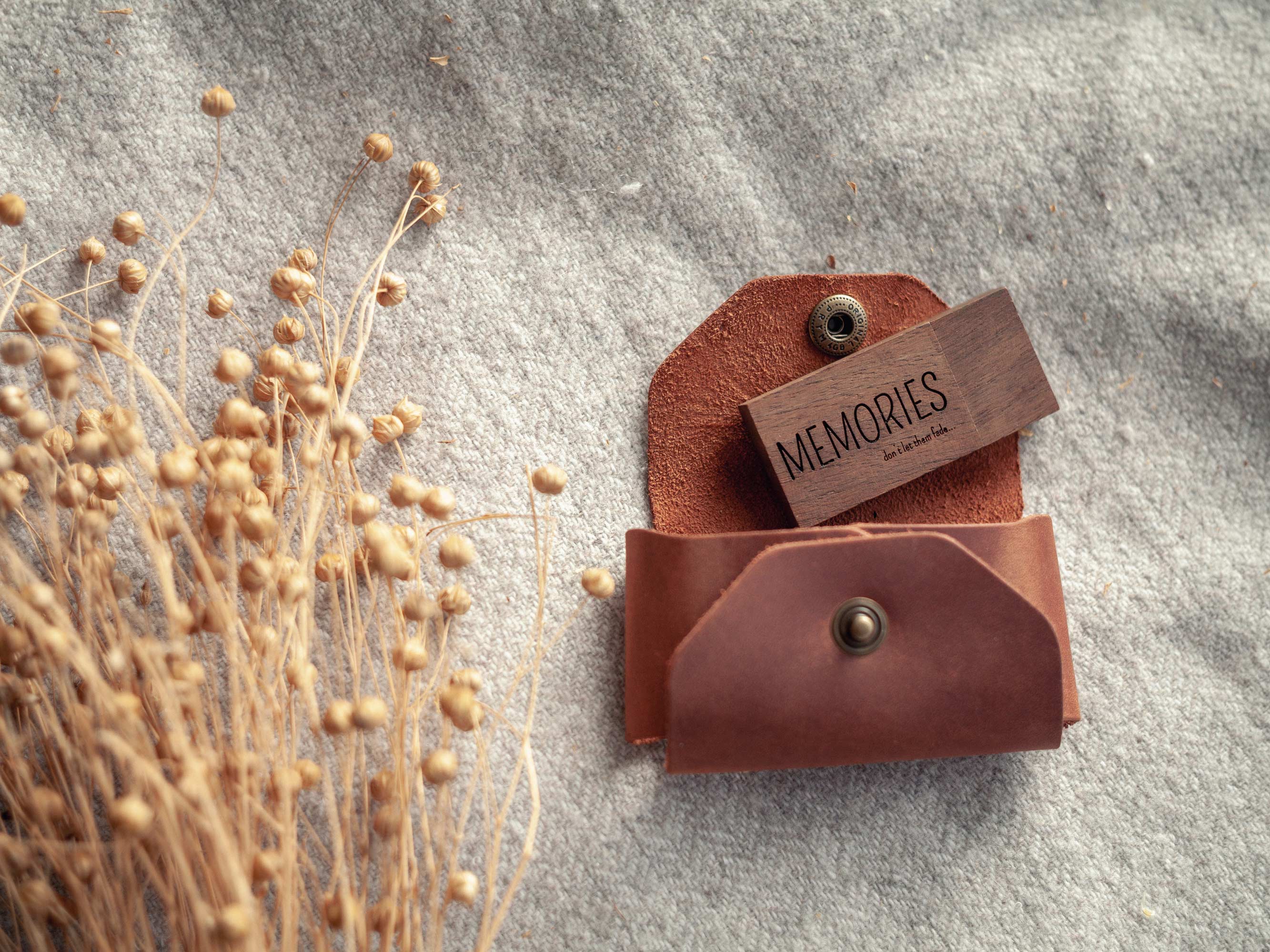 Open leather USB case with wooden flash drive inside, styled with dried grasses