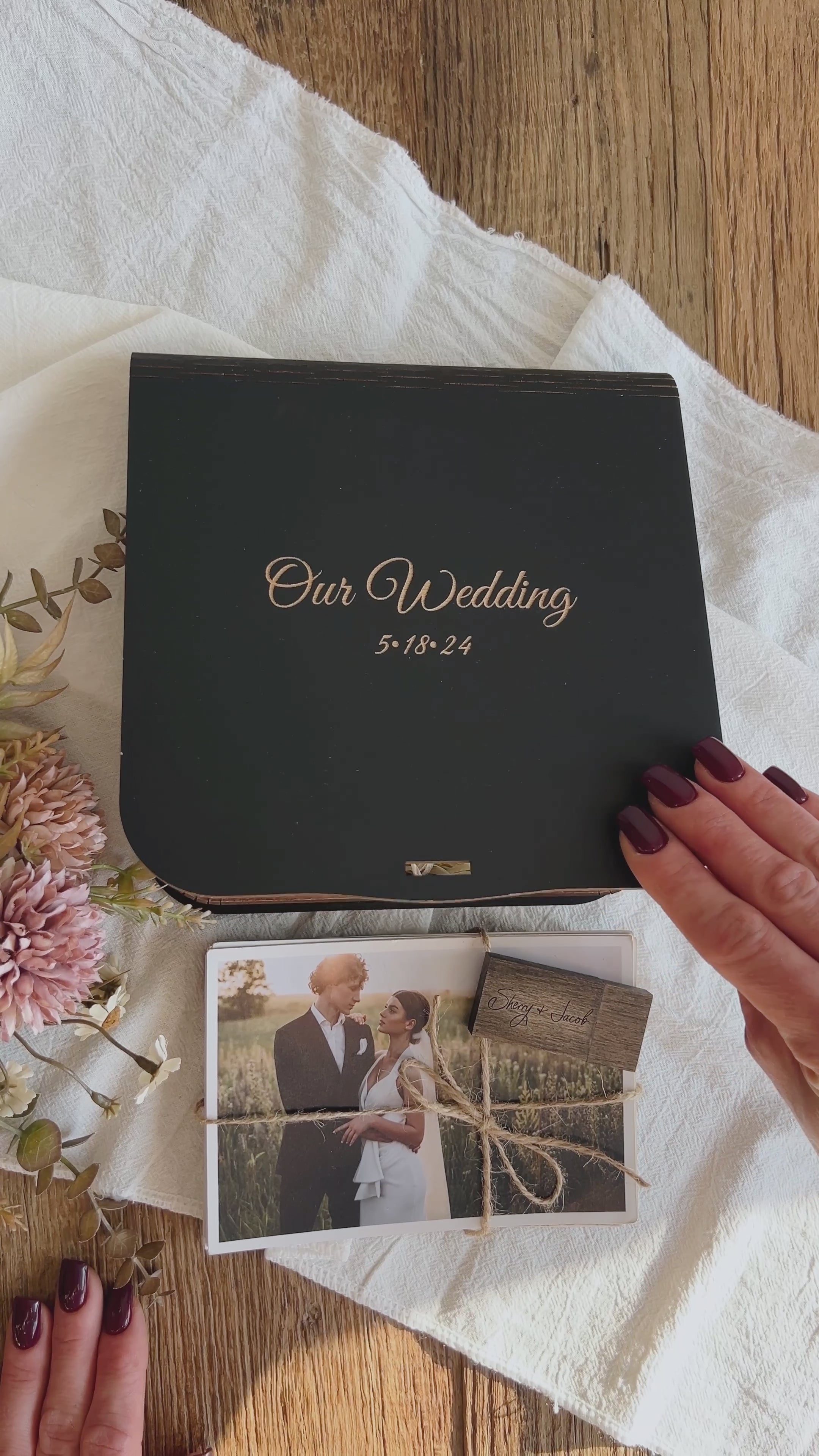Video shows unboxing of a personalized wedding photo box (black wood) with engraved “Our Wedding” lid, USB flash drive, and photo prints presentation.