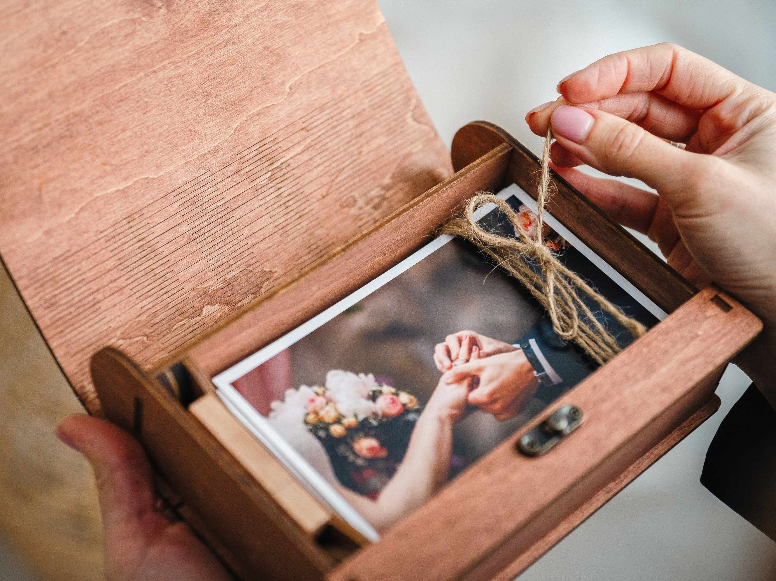 Hands opening teak photo box showing printed wedding photos and USB compartment