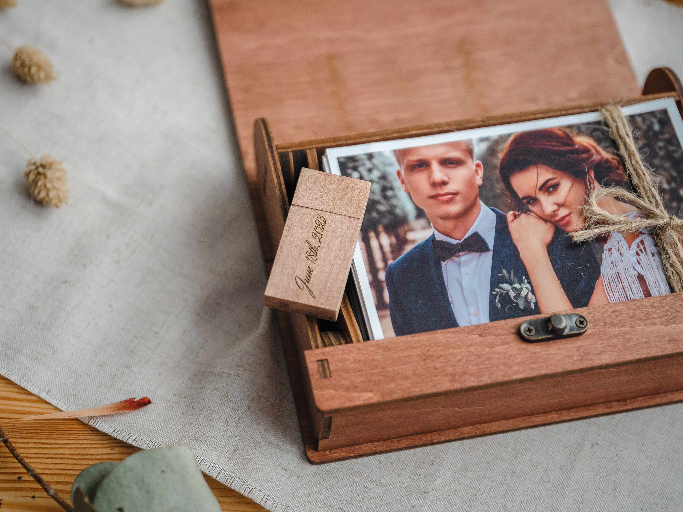 Open teak wedding photo box with prints inside and wooden USB placed next to photos