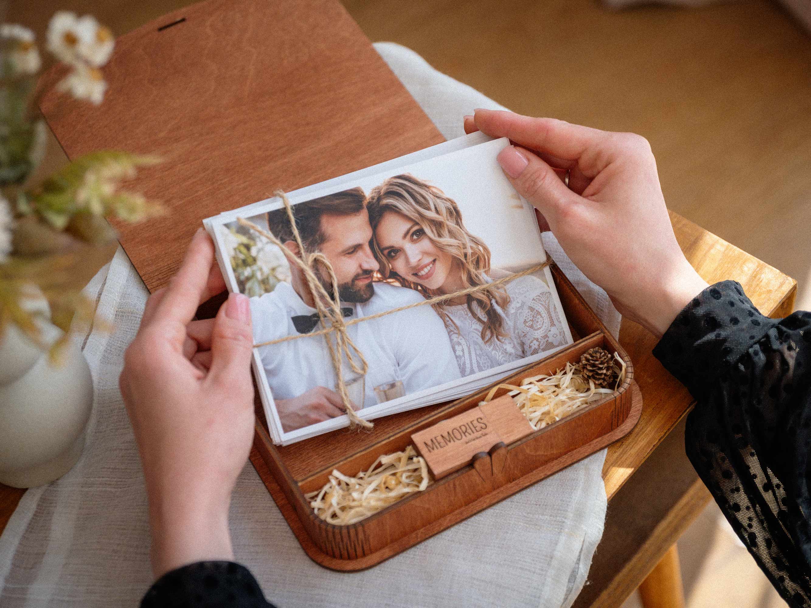 Open teak wedding photo box with USB and printed photos in hands