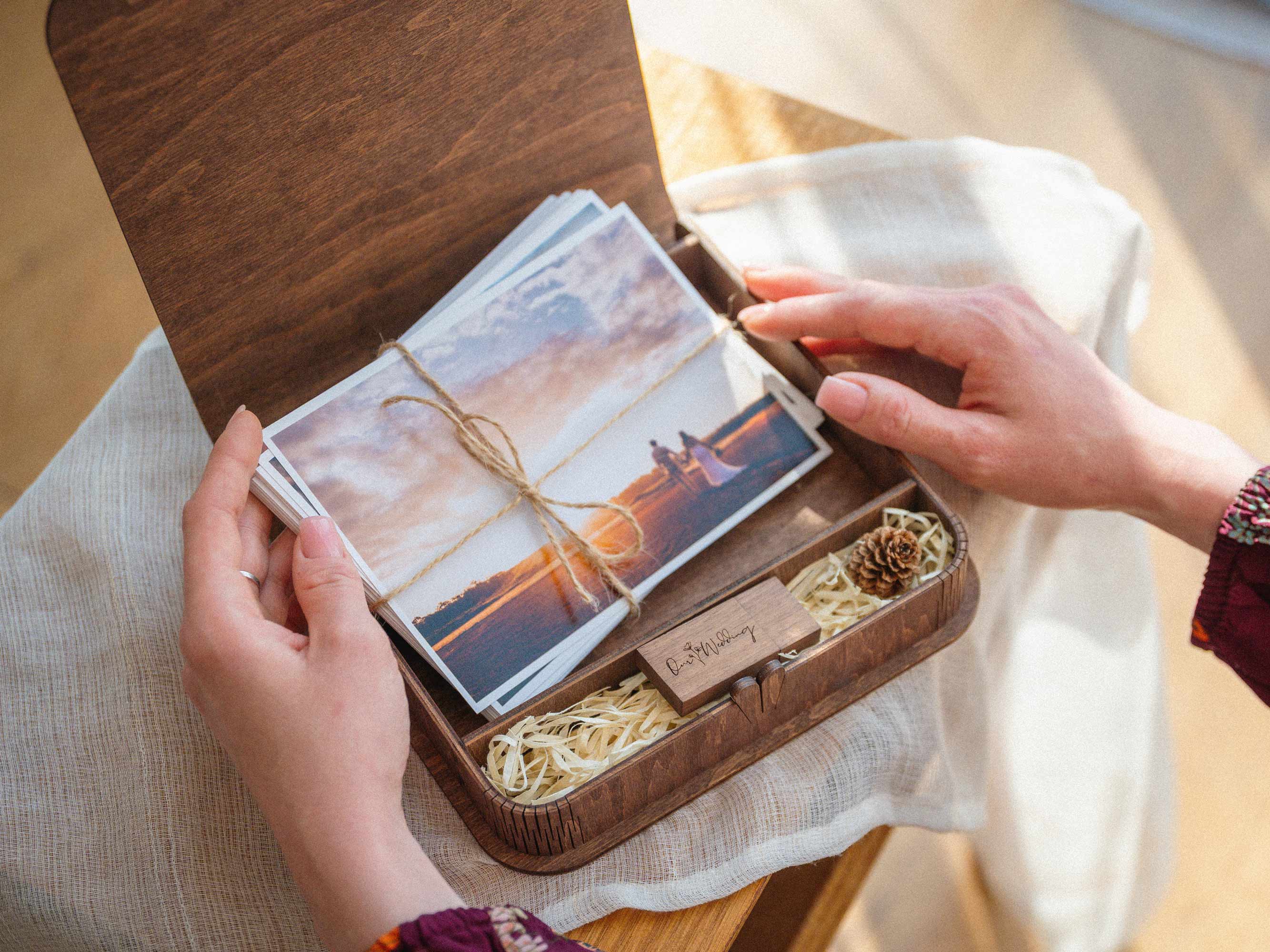 Open vintage style wooden photo box with USB and wedding prints, hands holding photo set
