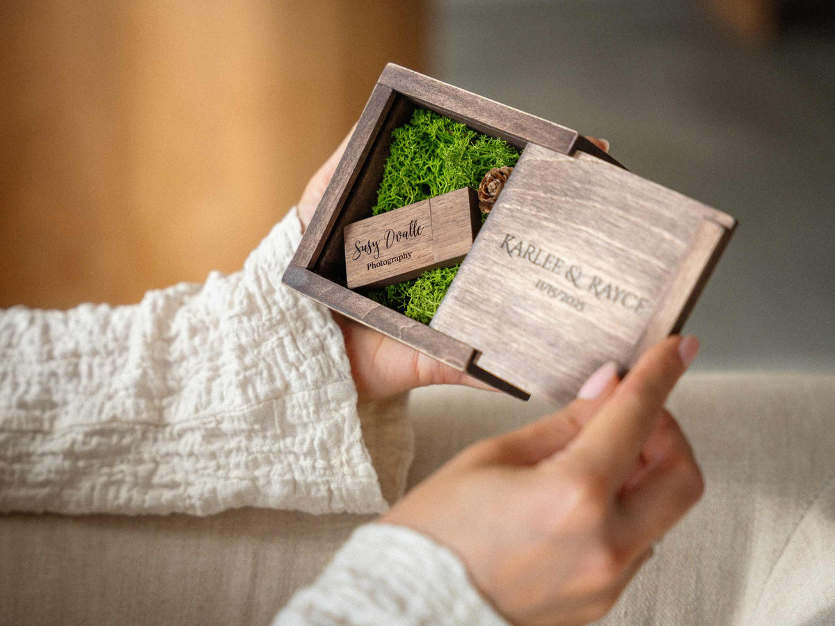 Personalized wooden USB box for wedding photographers, open with custom engraved USB flash drive and green moss, held in hands.